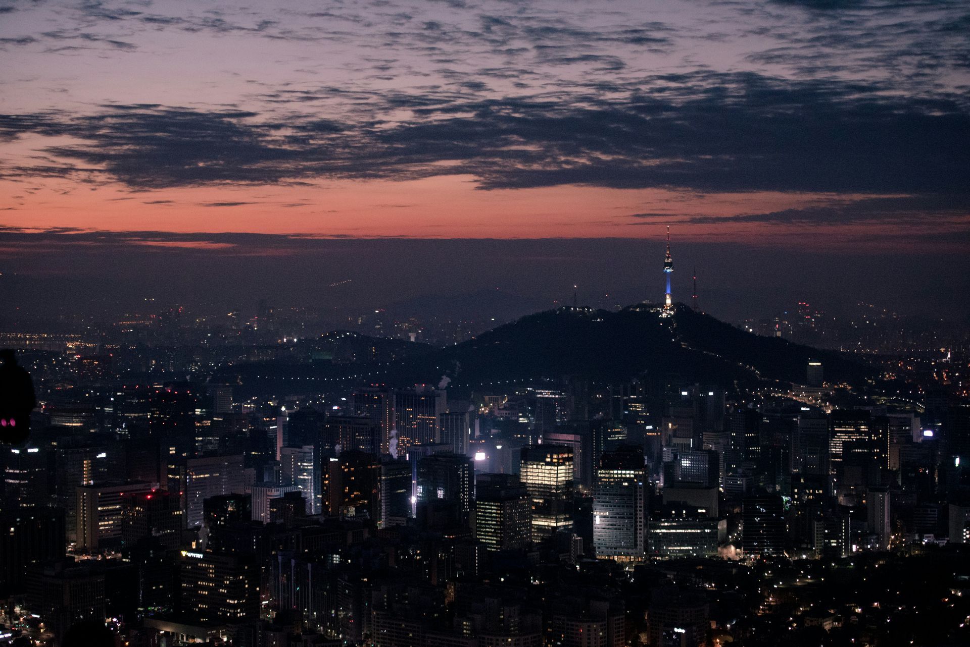 Seoul skyline at dusk with lights, topped by a mountain with a tower in South Korea.