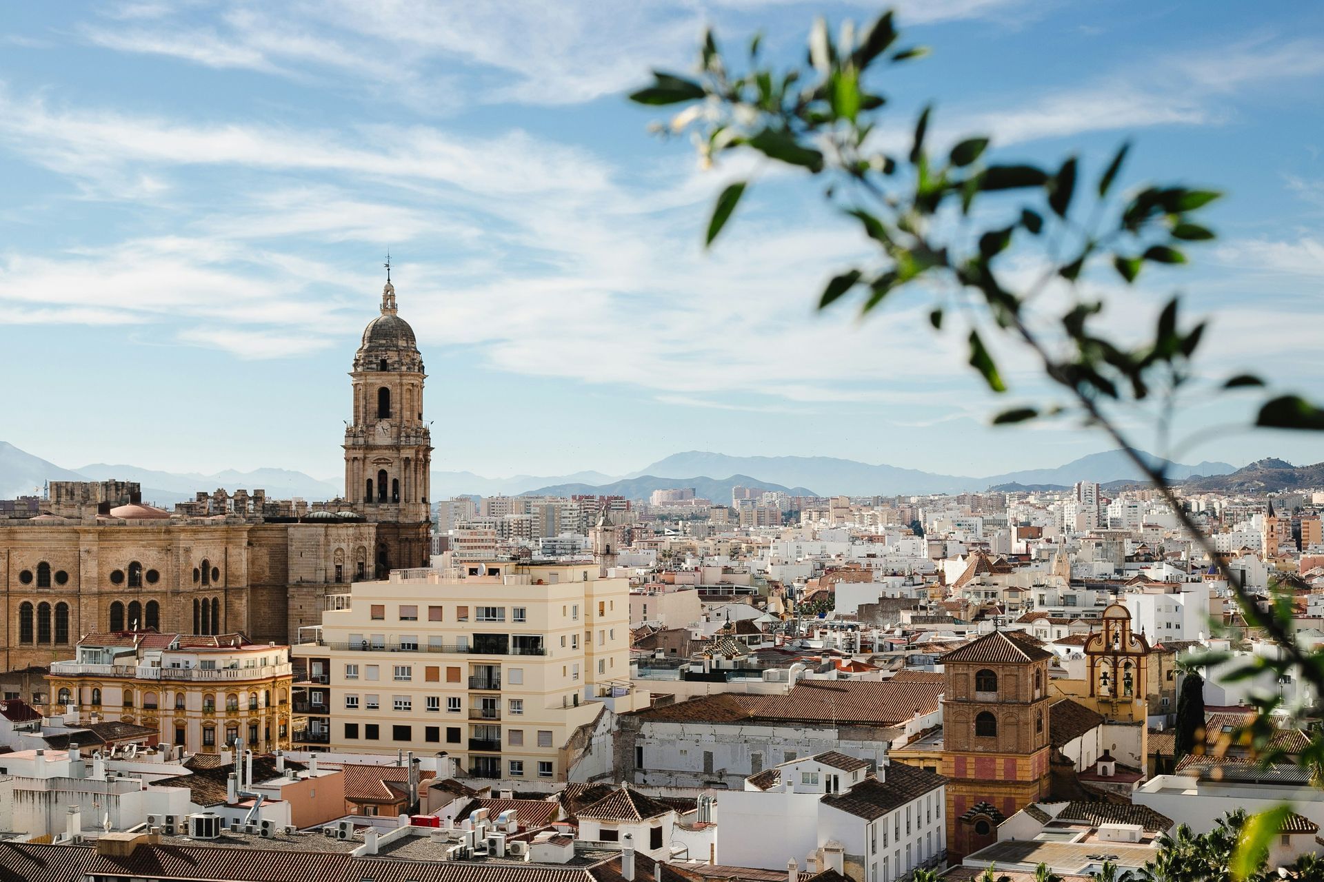 Cityscape of Malaga, Spain, with cathedral and distant mountains under a blue sky.