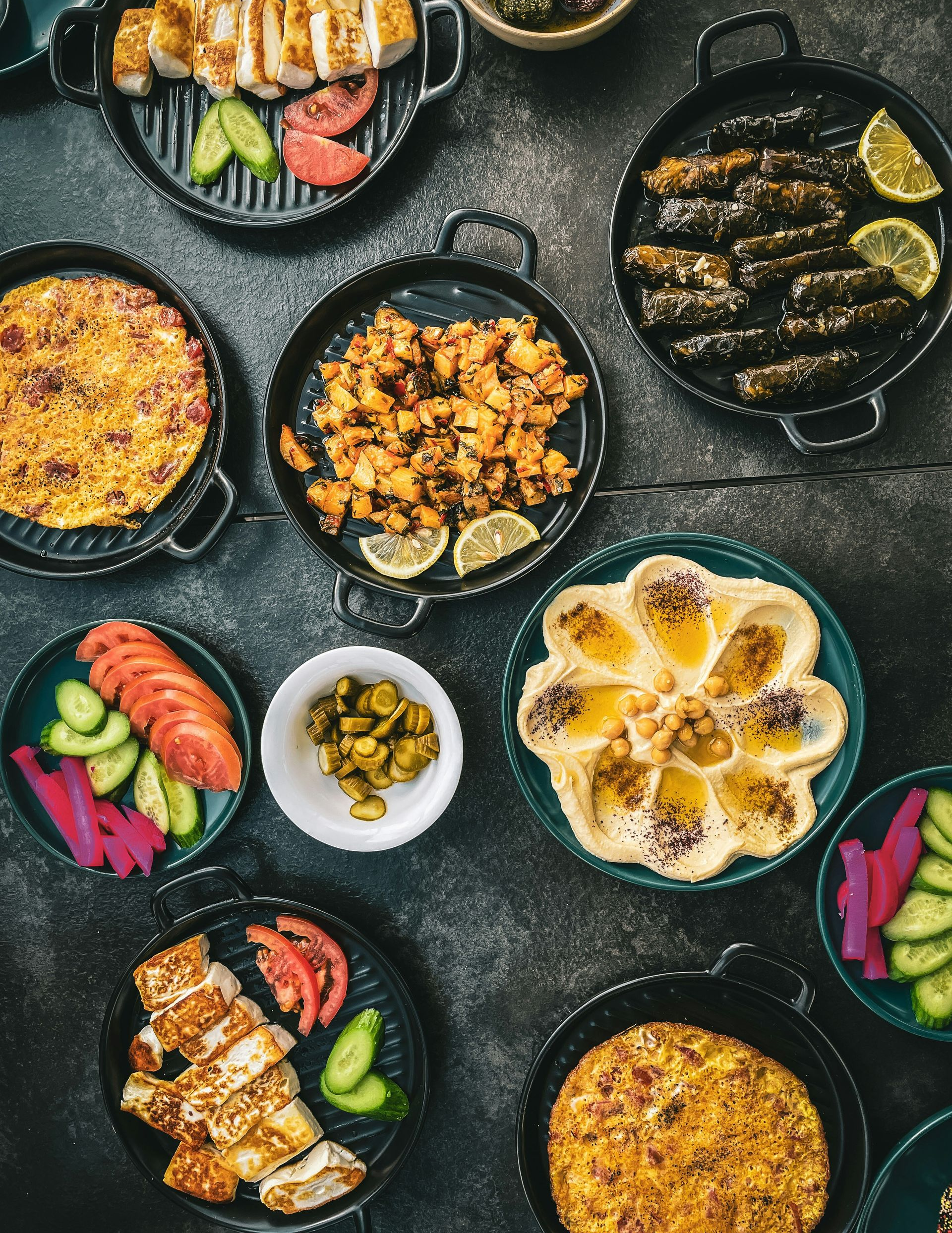 Overhead shot of Middle Eastern dishes on dark plates: hummus, stuffed grape leaves, chicken, vegetables in Jordan.