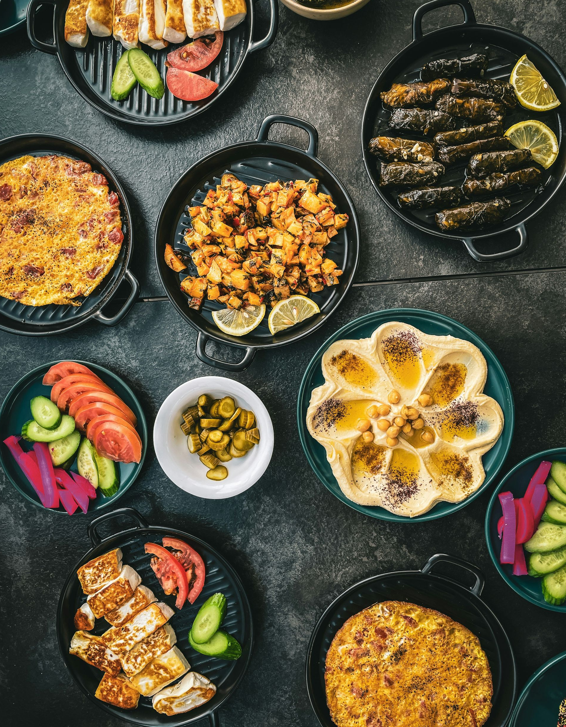 Overhead shot of Middle Eastern dishes on dark plates: hummus, stuffed grape leaves, chicken, vegetables in Jordan.