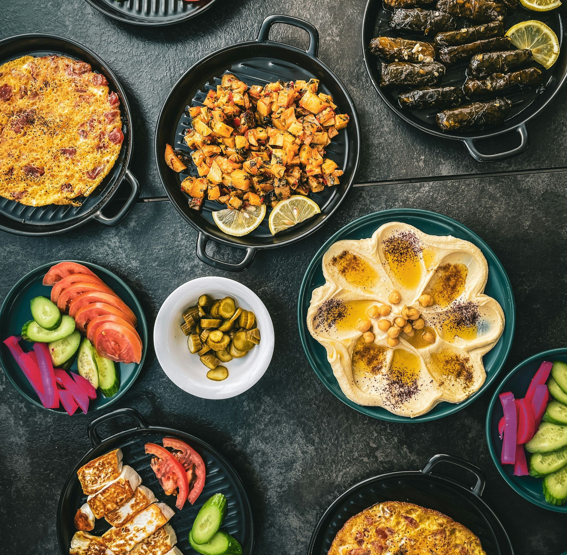 Overhead shot of Middle Eastern dishes on dark plates: hummus, stuffed grape leaves, chicken, vegetables in Jordan.