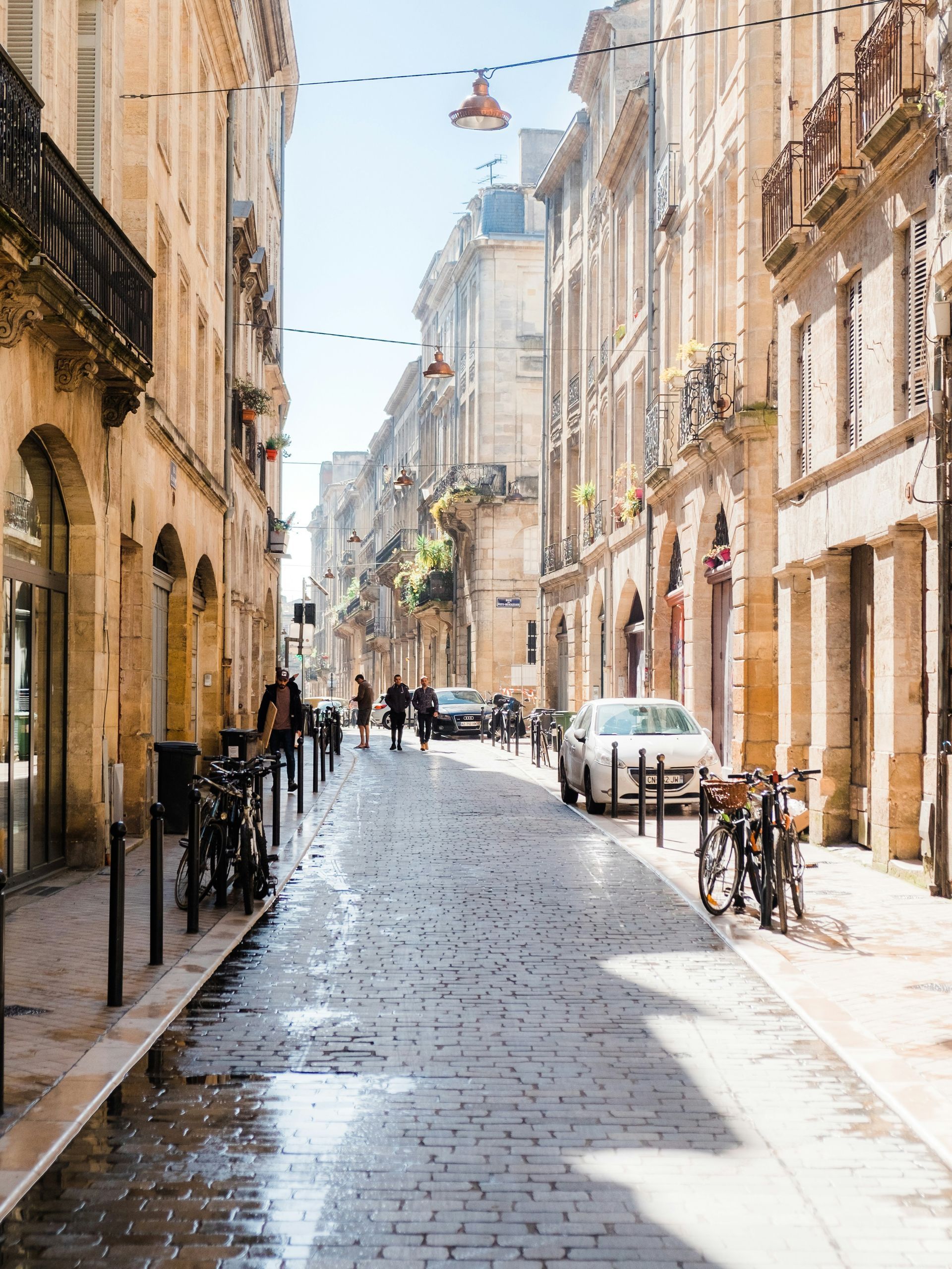 A narrow cobblestone street in Bordeaux, France with cars parked on the side.