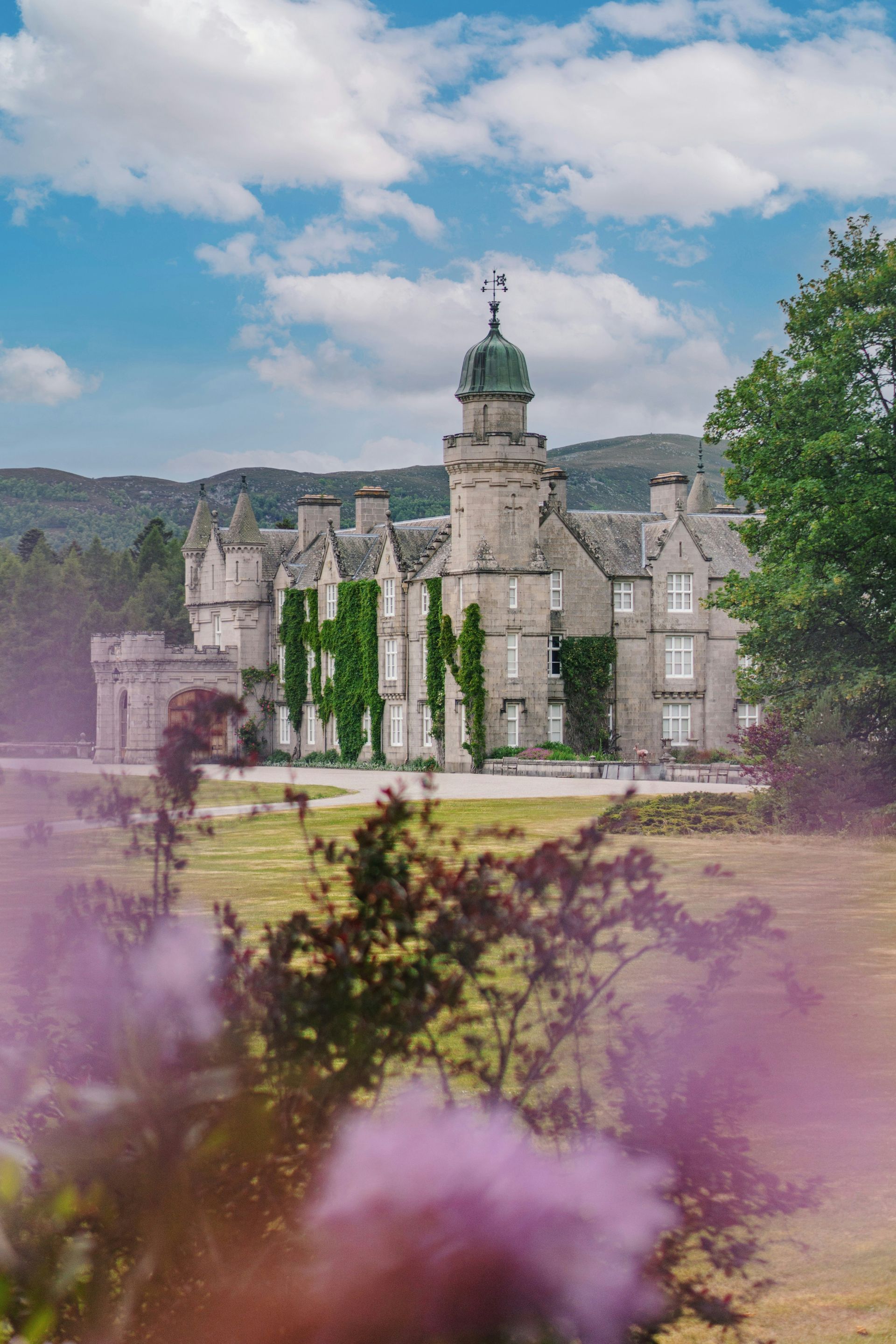 Balmoral Castle with ivy, tower, green grass, and purple smoke on a sunny day in Scotland.
