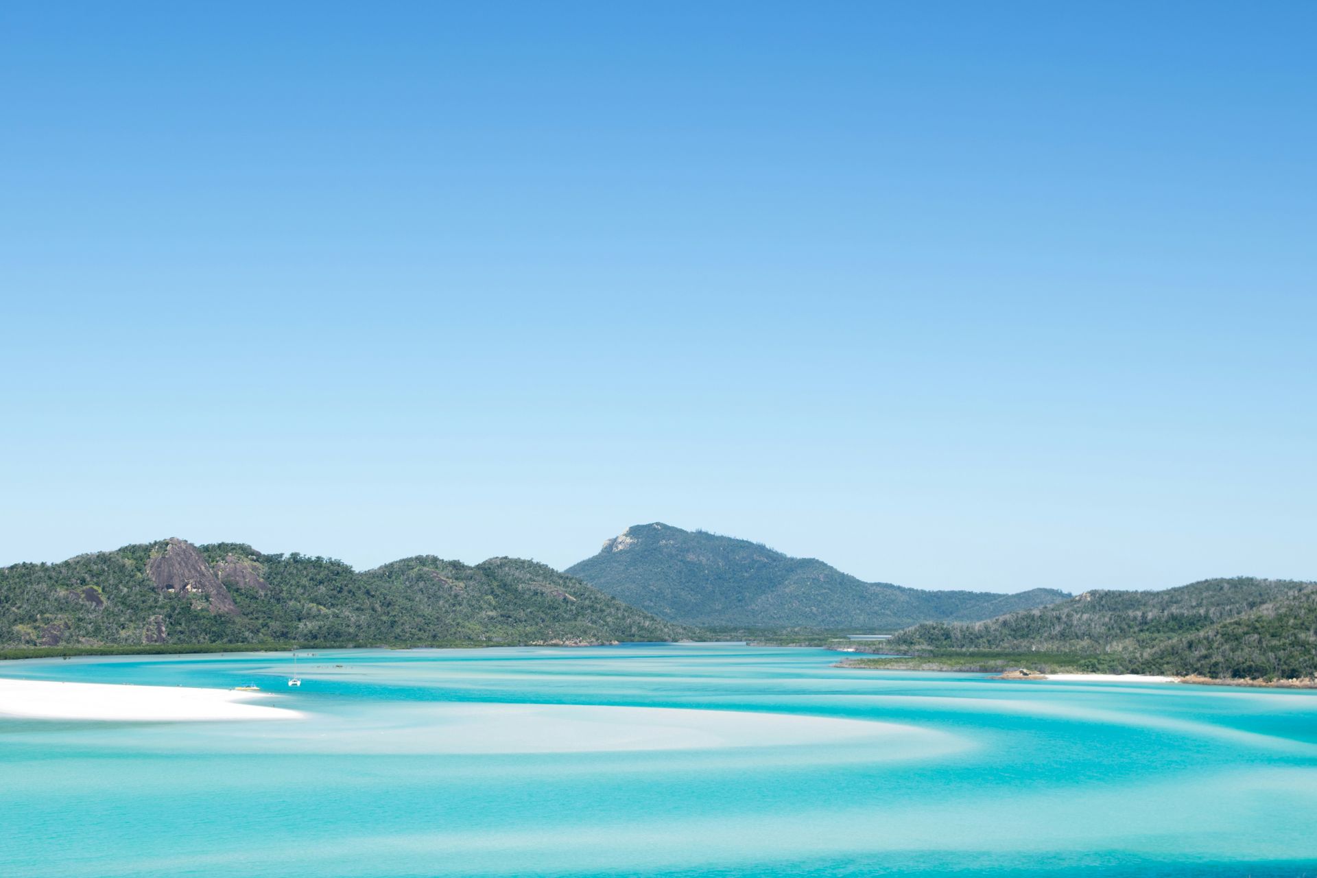 A large body of water with mountains in the background and a blue sky in the Whitsundays, Australia. 