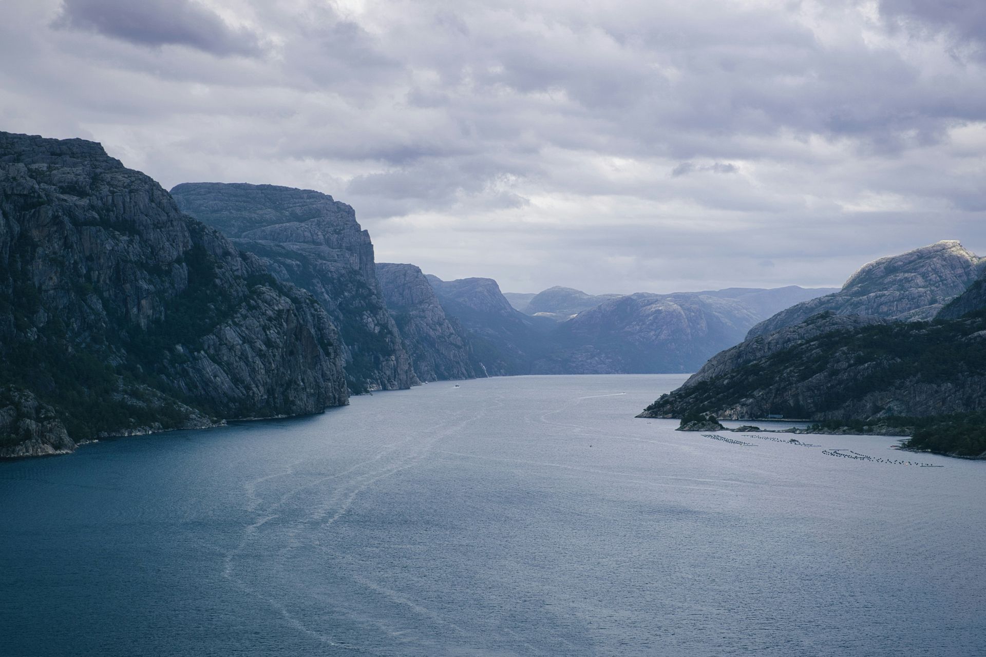 Lysefjord under a cloudy sky, framed by towering gray cliffs and speckled mountains in Norway.