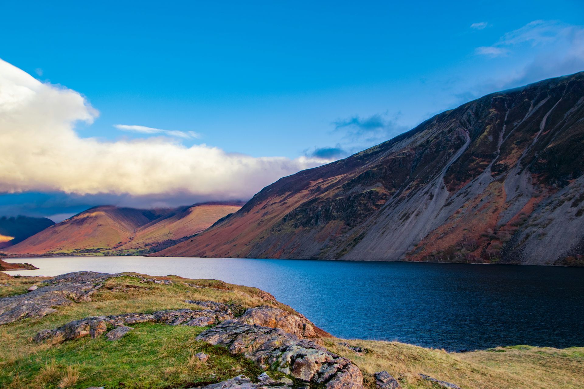 Lake surrounded by mountains under a blue sky with some clouds in the Lake District, England.