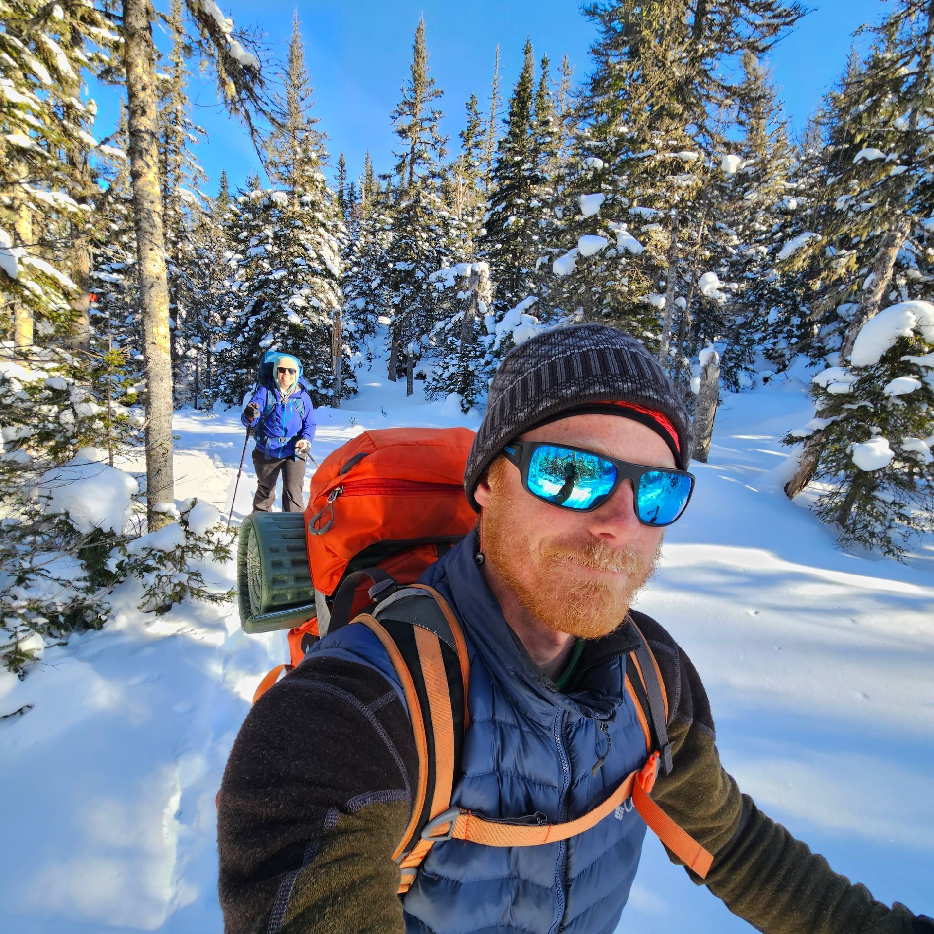 A man wearing sunglasses and a hat is standing in the snow