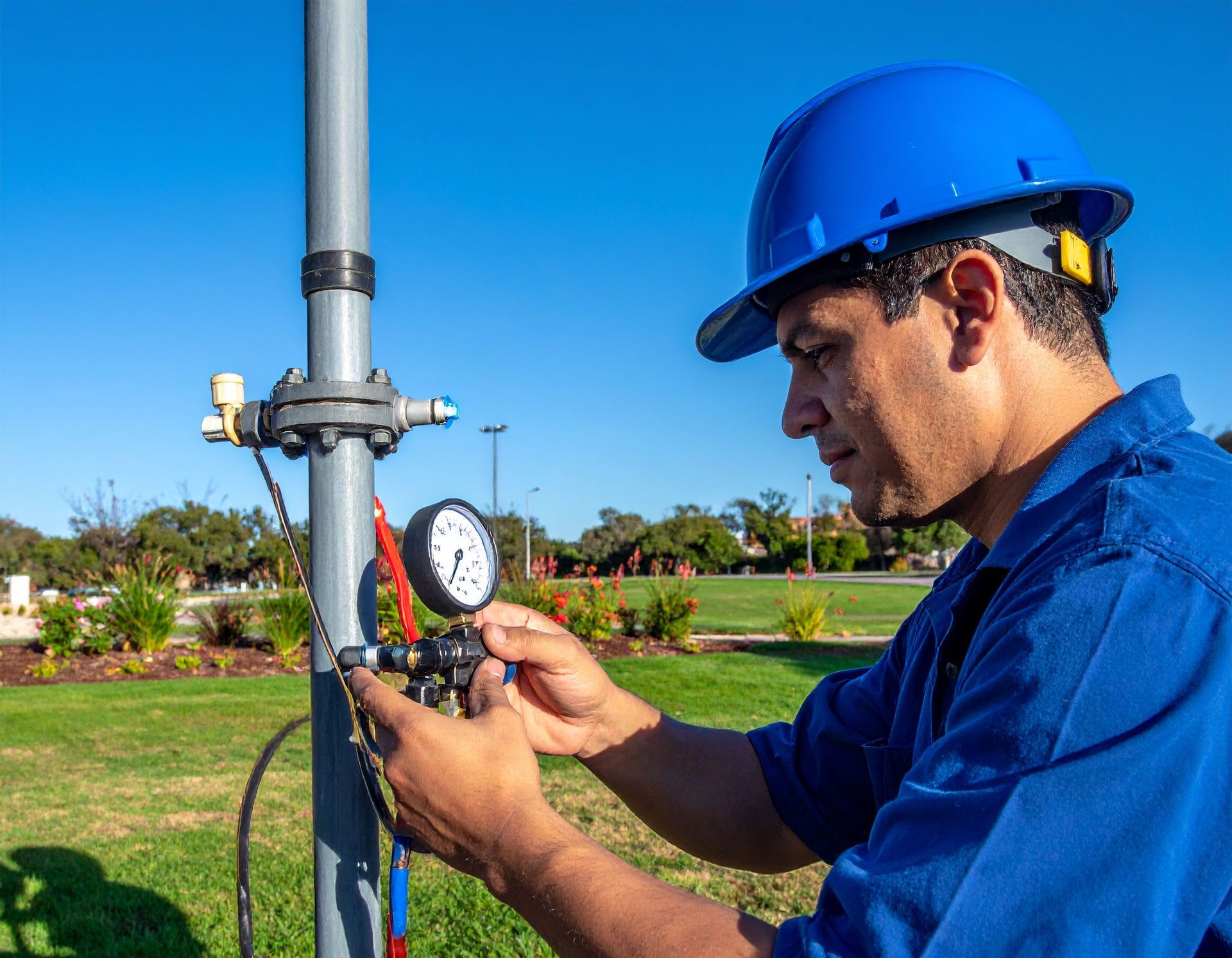 Worker in blue hard hat checking a pressure gauge on a pipe outdoors