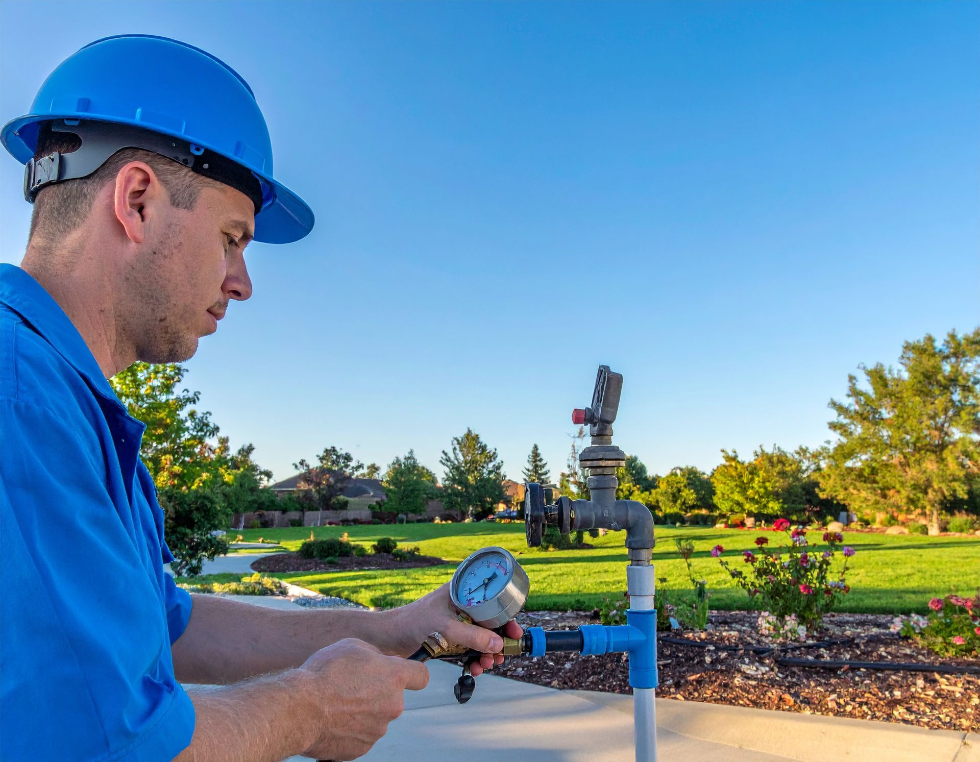 Worker in blue hard hat checking a sprinkler valve outdoors on a sunny day