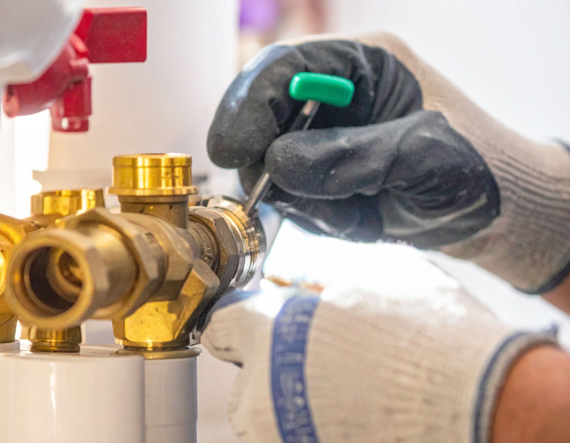 Gloved hands adjusting a brass valve assembly with a green-handled tool