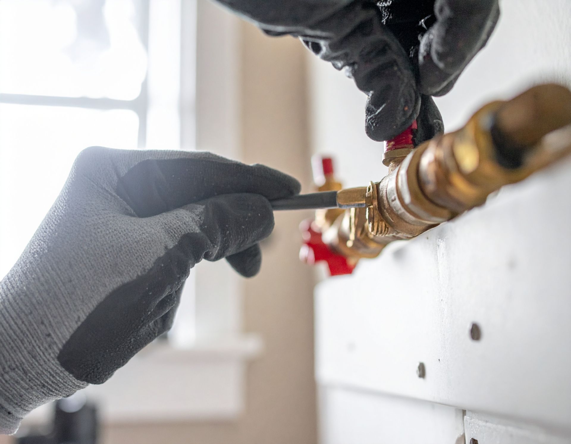 Gloved hands adjusting a brass plumbing valve with a screwdriver