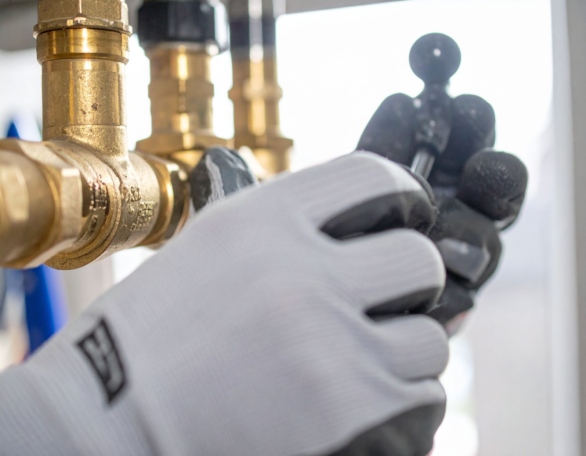 Gloved hands adjusting brass pipes and fittings on a plumbing system