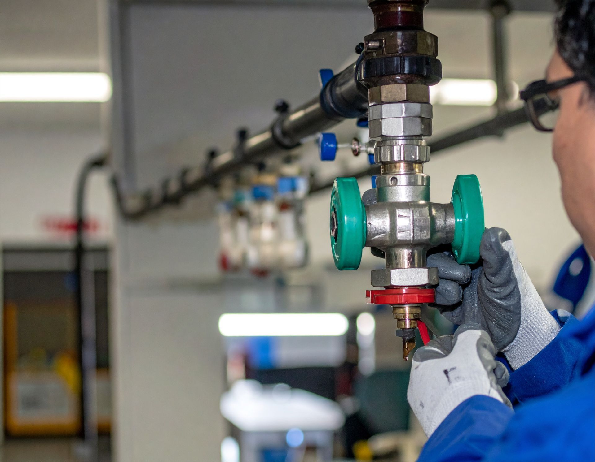 Gloved technician adjusts a green valve on a metal pipe in an industrial facility