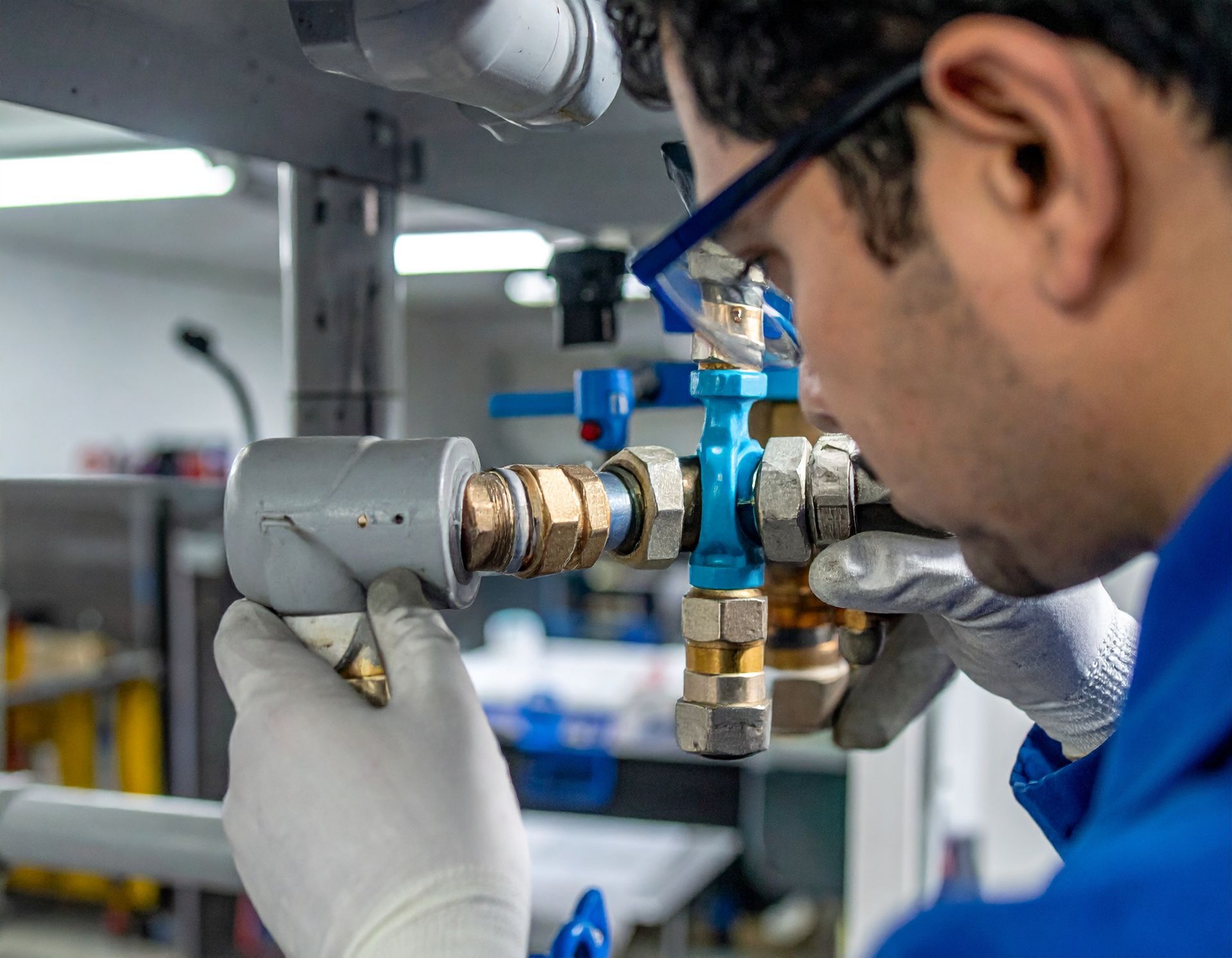 Technician in gloves inspecting a blue valve and brass pipe assembly in an industrial setting