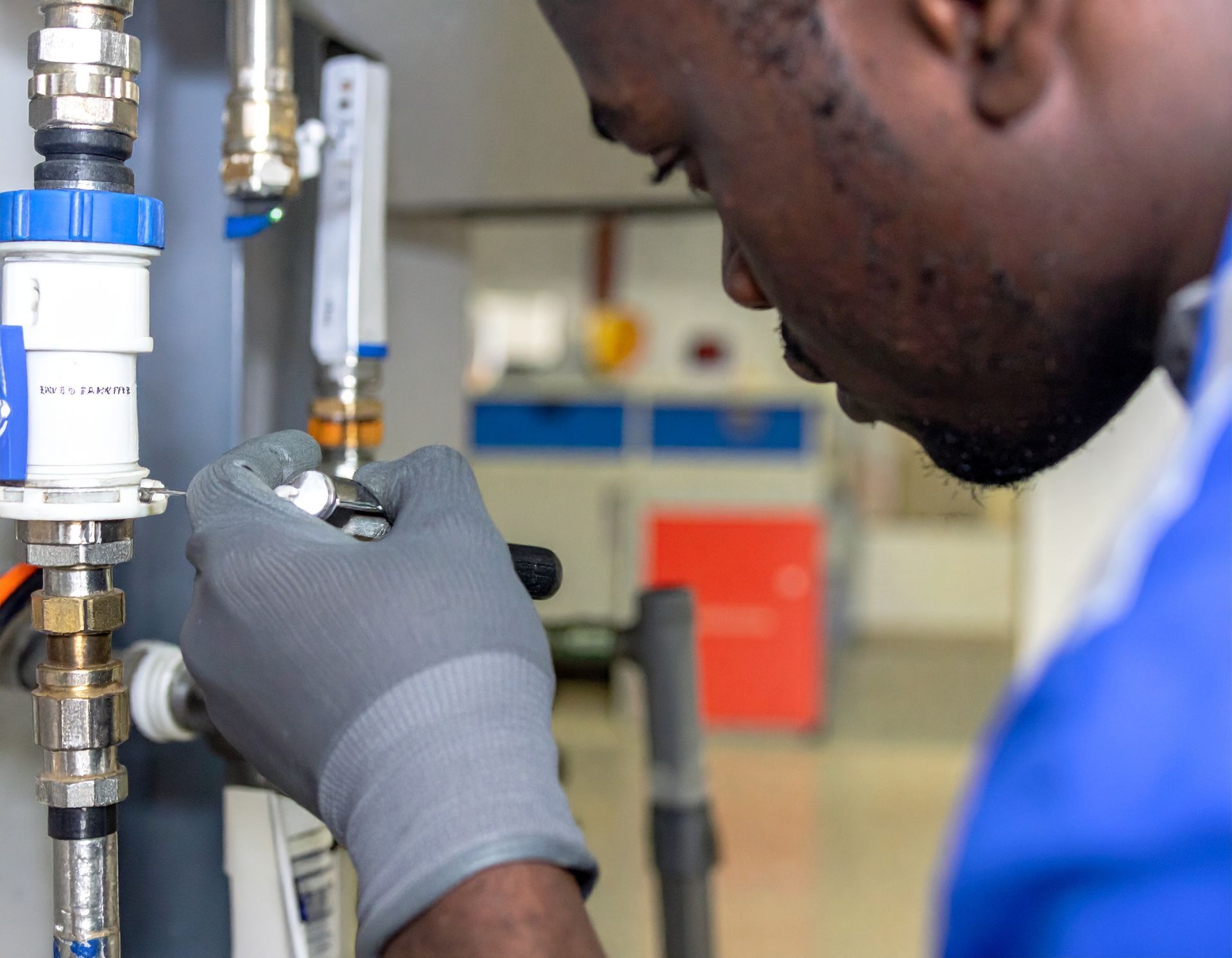 Technician in blue uniform and gray gloves inspecting a pipe connection in an industrial setting