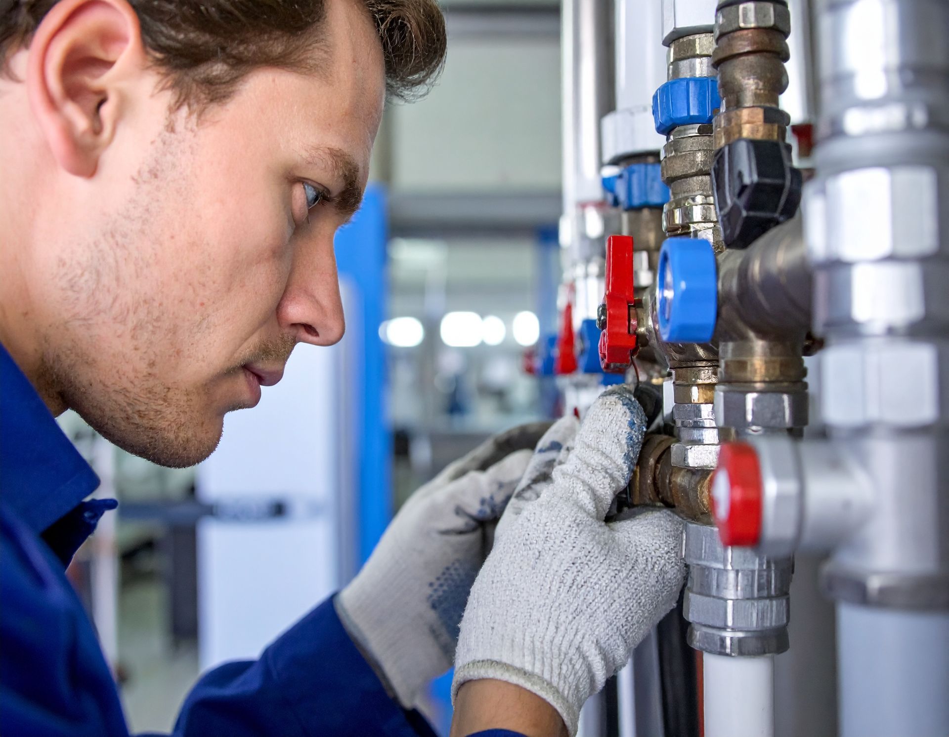 Technician in blue uniform adjusting valves on industrial piping with a wrench