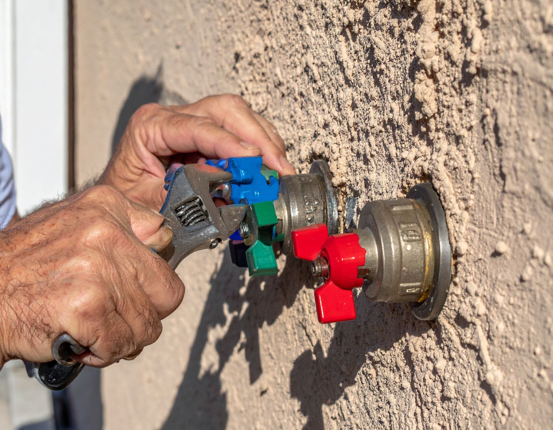 Hand connecting a blue hose fitting to a red wall-mounted valve outdoors on a stucco wall