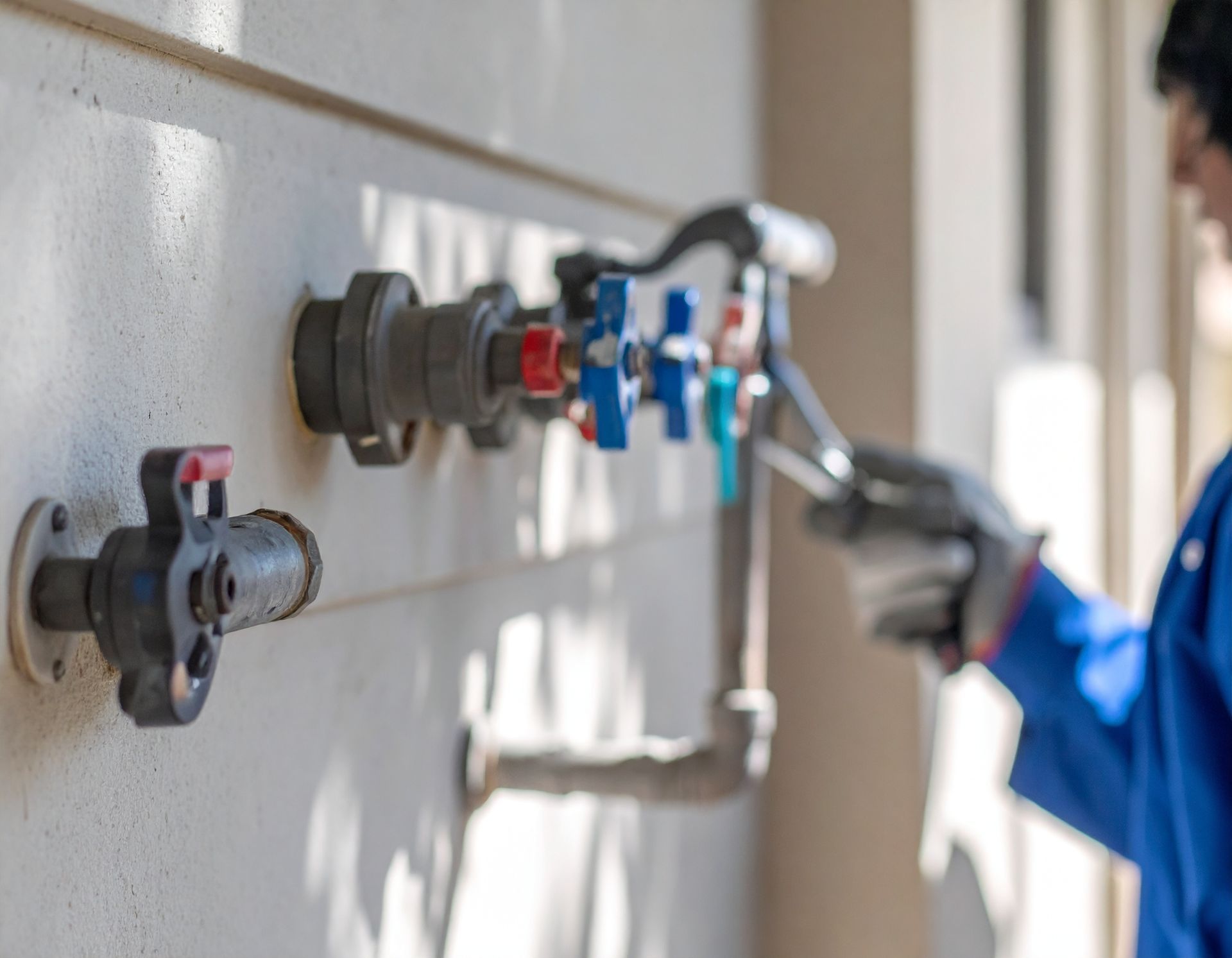 Worker tightening plumbing valves on a wall-mounted pipe system indoors