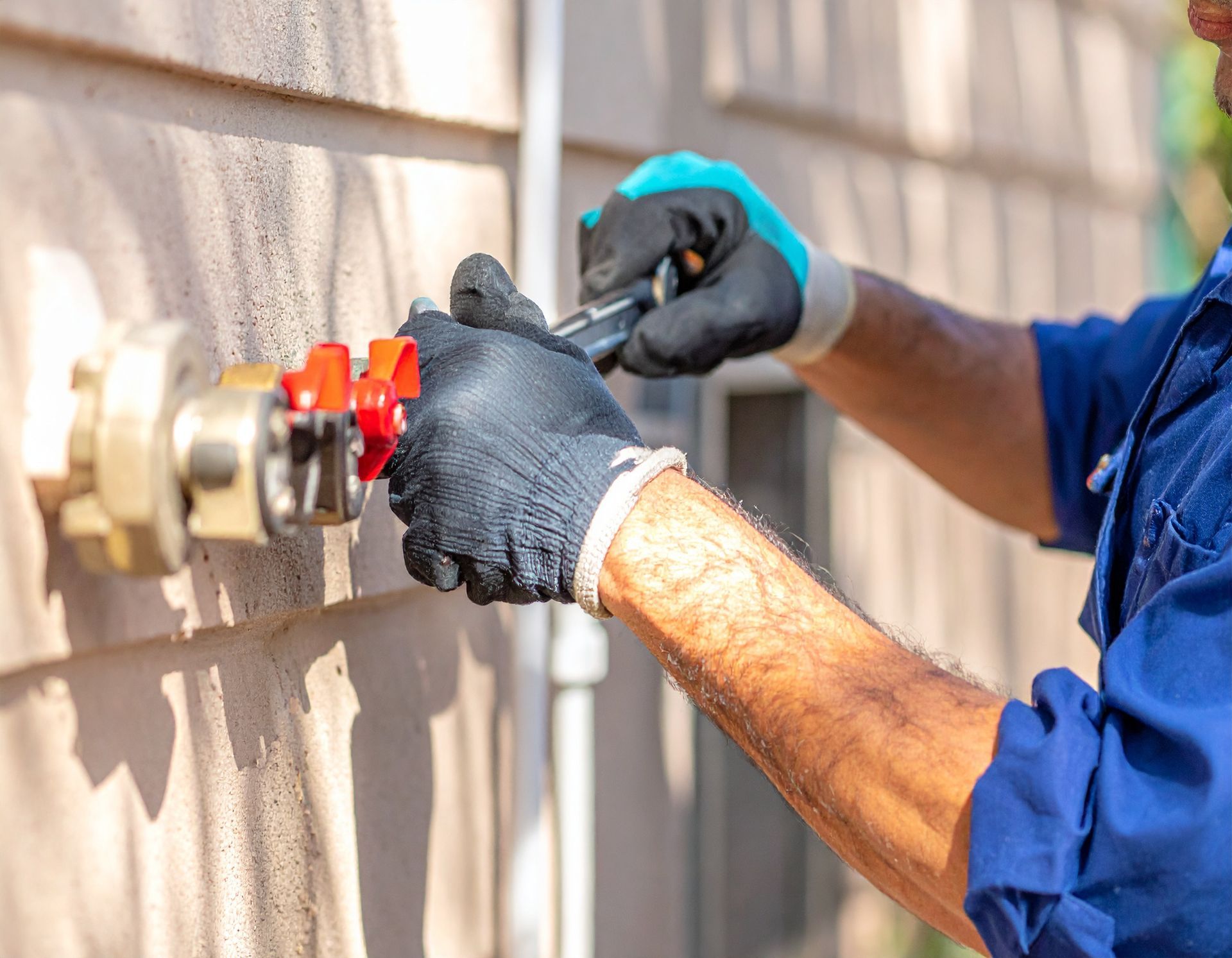 Gloved worker tightening a red valve on an outdoor gas or water pipe