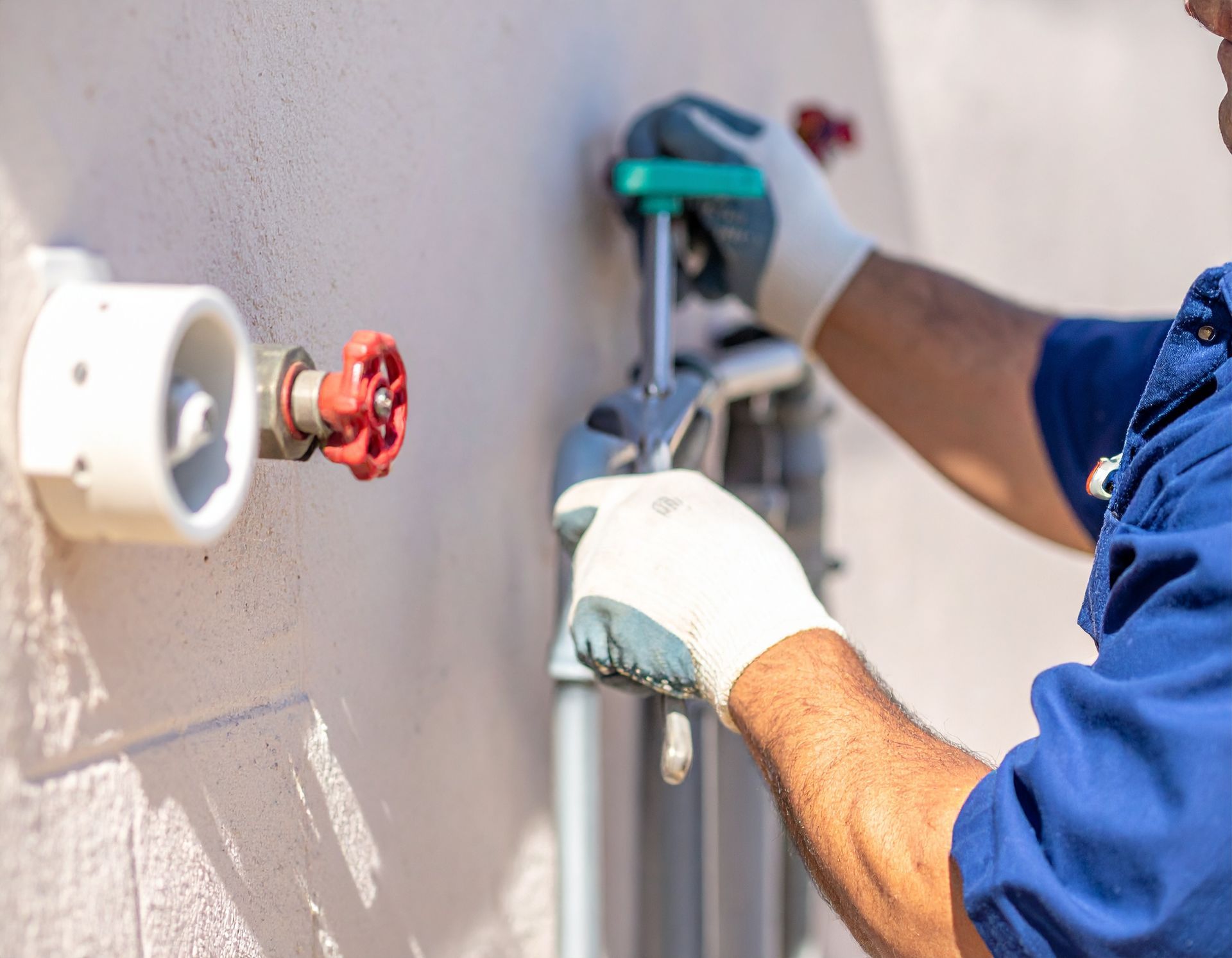Worker in blue shirt and gloves using a drill to repair a wall-mounted pipe fixture