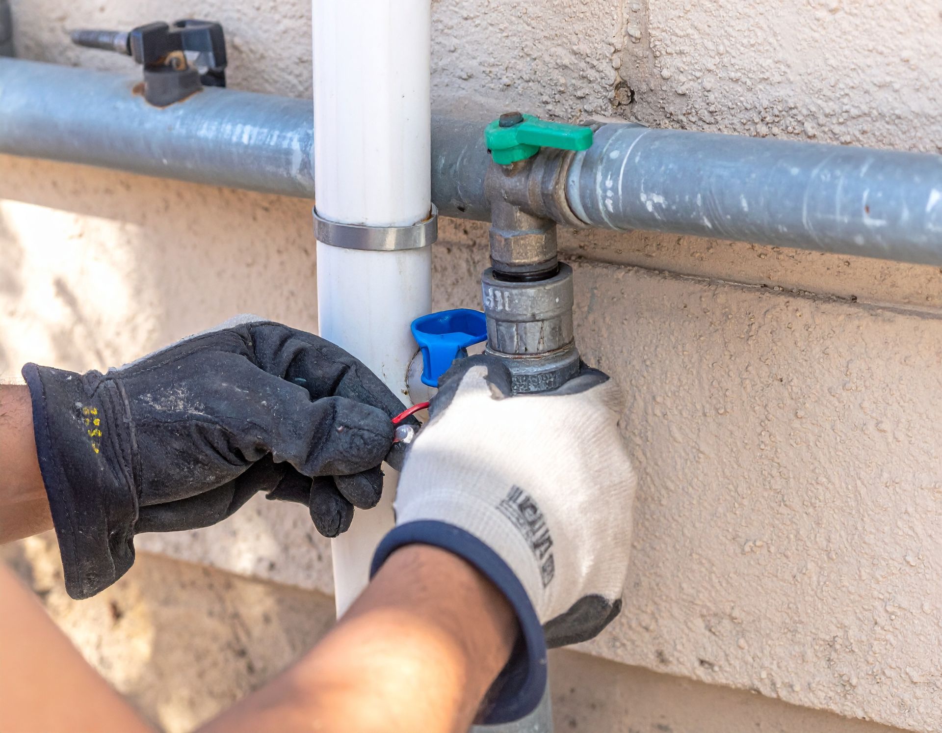 Gloved hands turning a shutoff valve on an outdoor water pipe