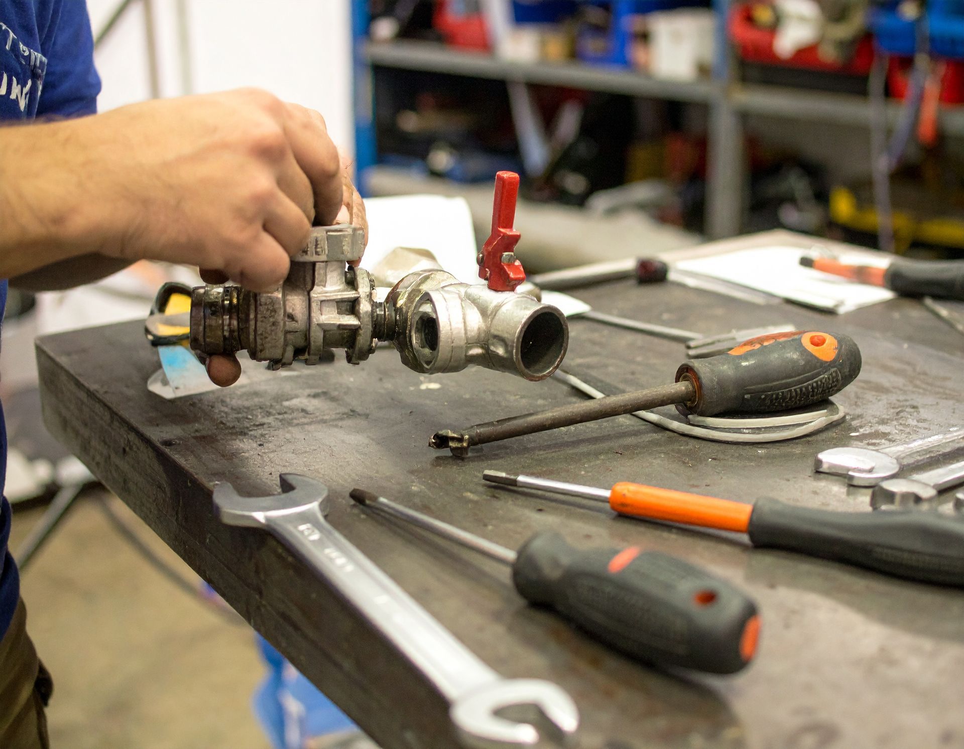Person working on a metal part with tools on a workbench in a workshop.