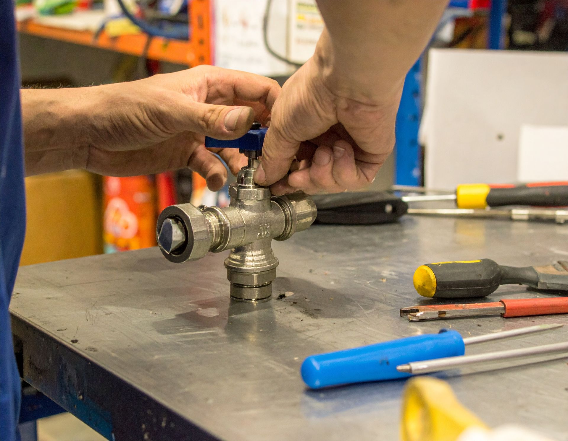 Hands repairing a metal valve assembly on a workbench with tools nearby