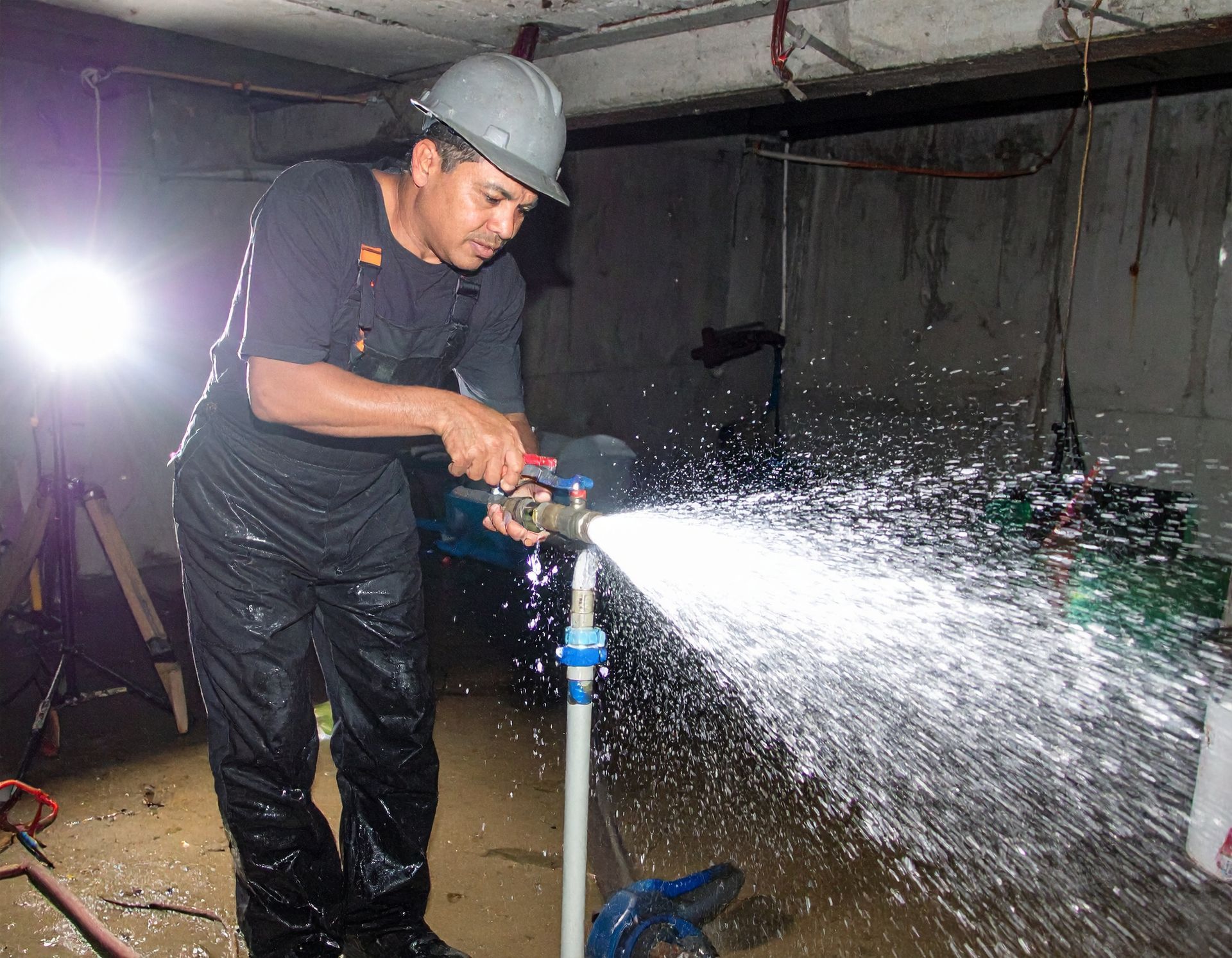 Worker in hard hat spraying water from a hose in a wet indoor construction area