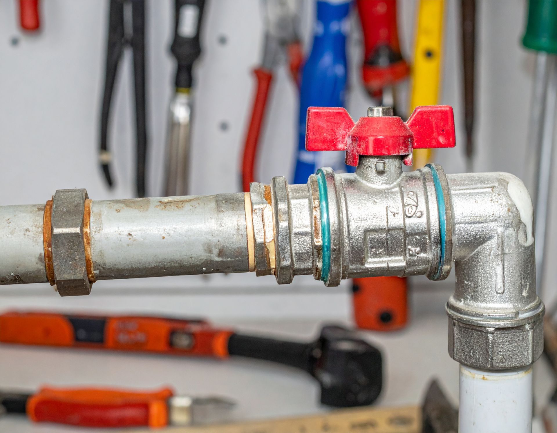 Close-up of a metal pipe with a red-handled valve in a workshop, with tools blurred in the background