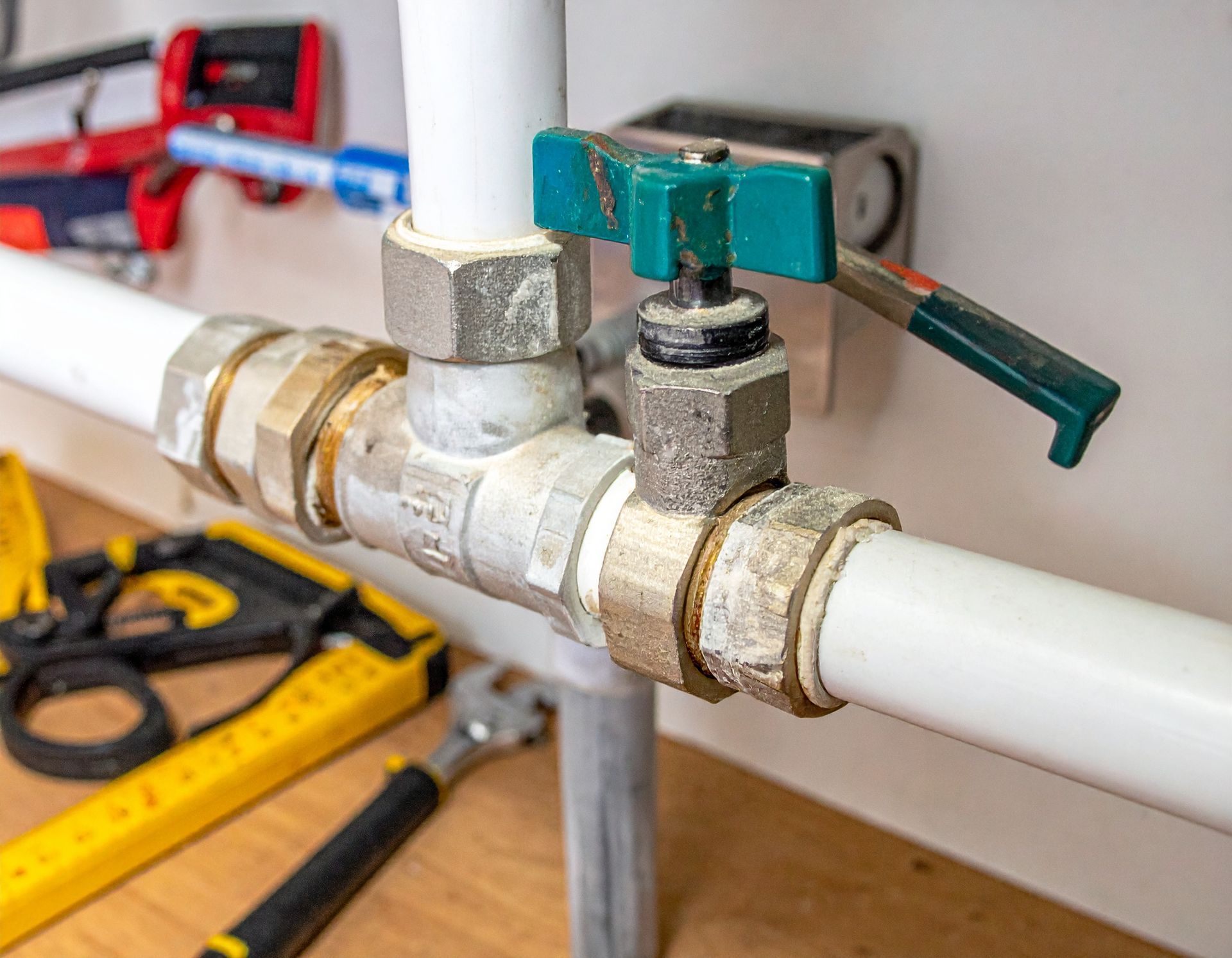 Close-up of a white PVC pipe with a green-handled valve and brass fittings on a workbench.
