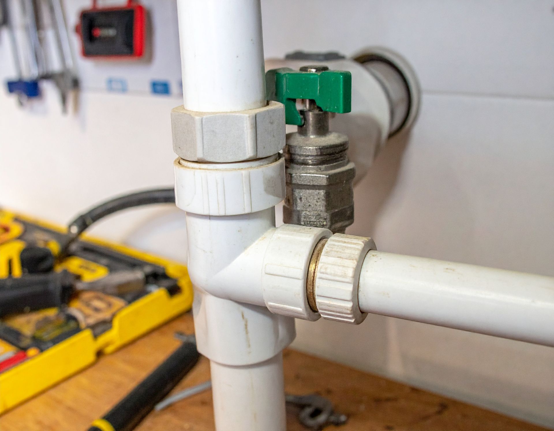 White PVC pipe with a green shutoff valve in a workshop, with a yellow toolbox in the background