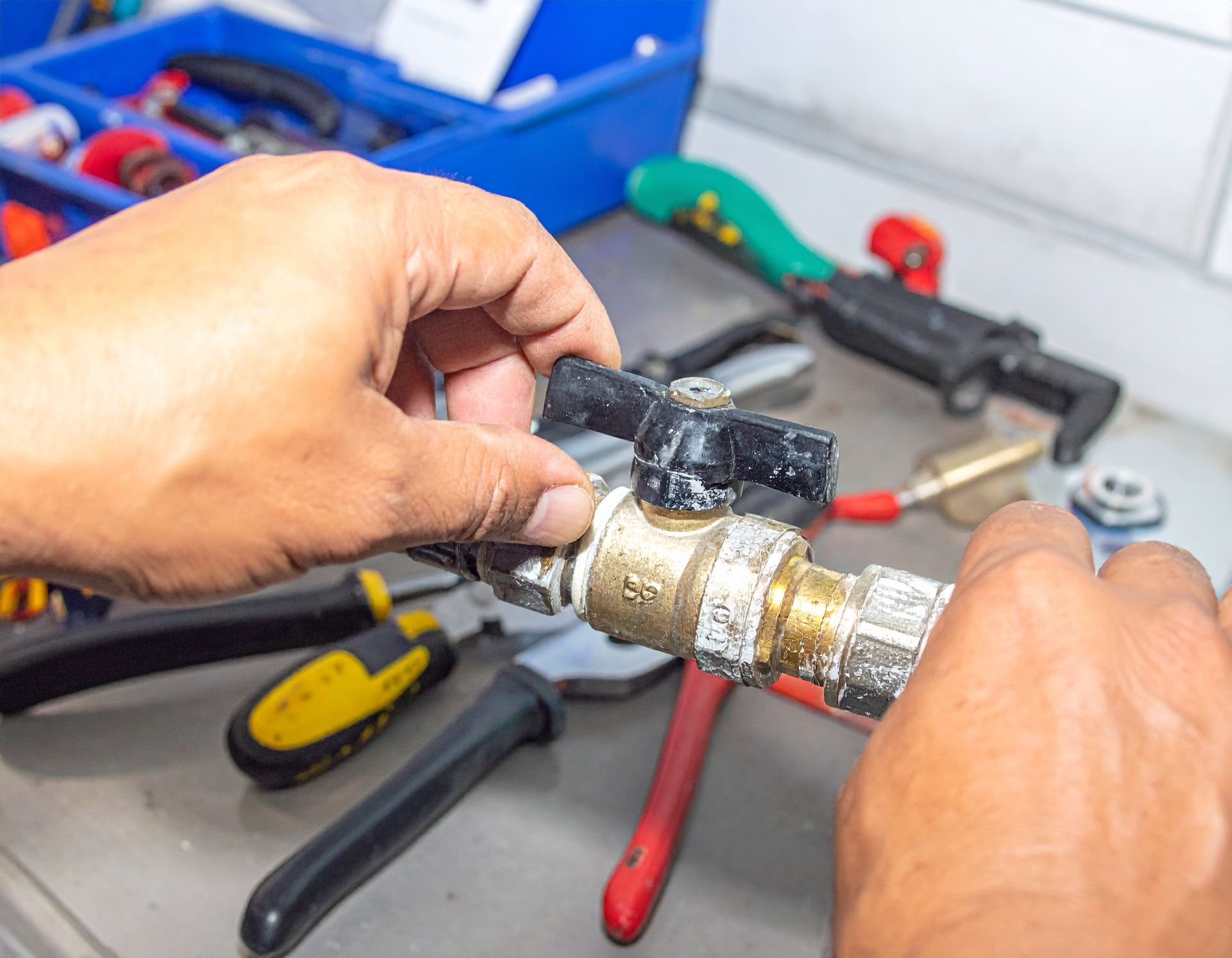 Hands repairing a brass pipe fitting on a workbench with tools scattered nearby