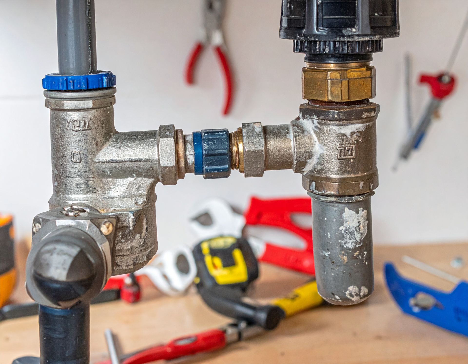 Two metal plumbing valves with blue caps on a workbench, surrounded by hand tools.