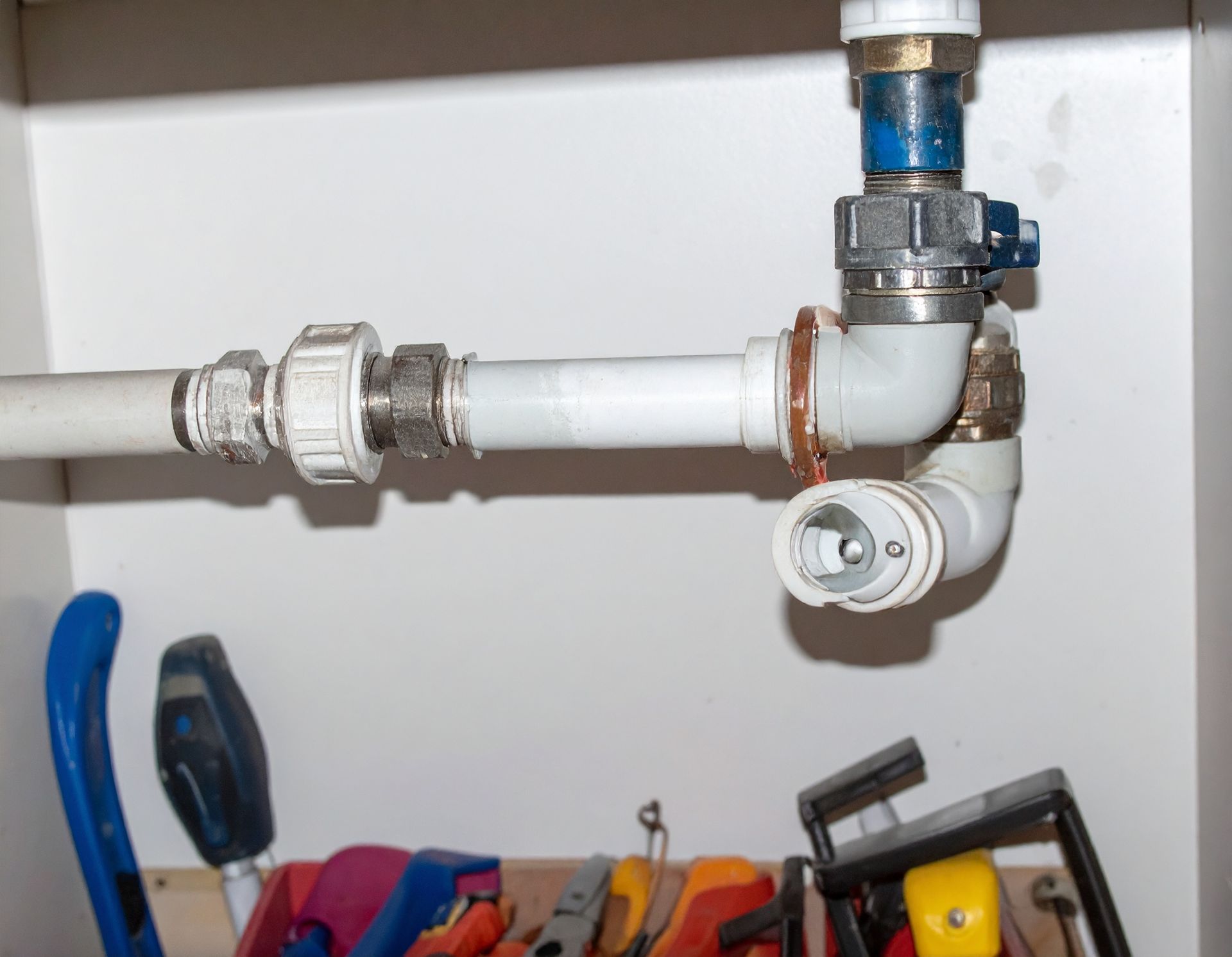 White PVC plumbing pipes and valves mounted on a wall above a shelf of tools.