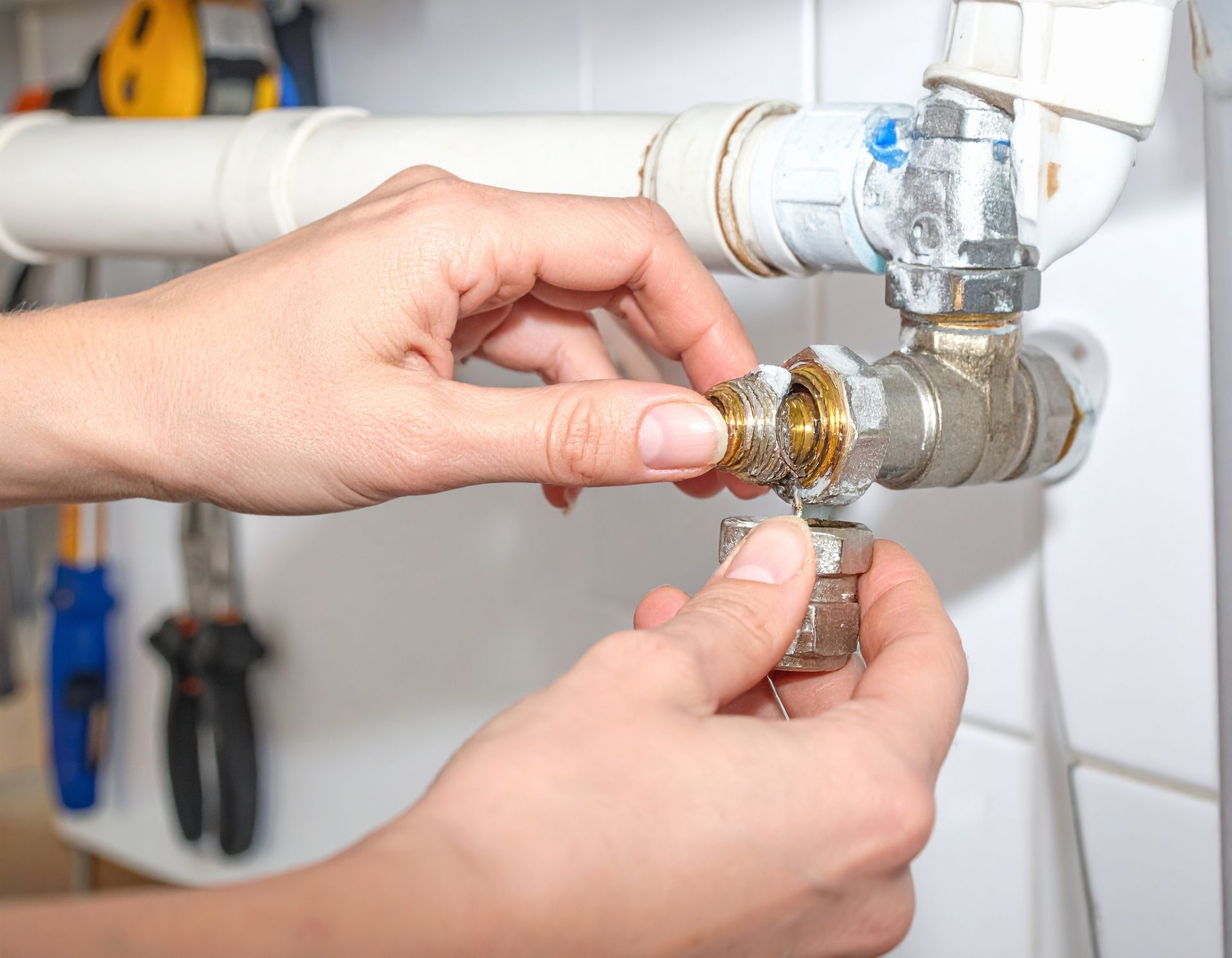 Hands tightening a faucet connector under a sink with a wrench, plumbing repair in progress
