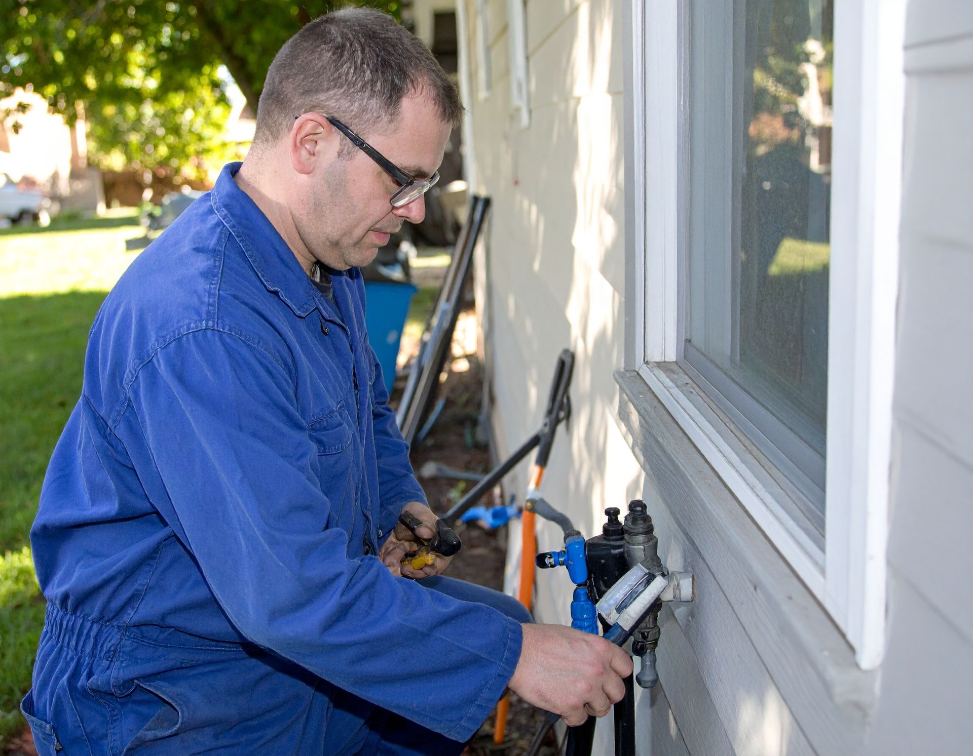 Worker in blue coveralls using a tool to repair an exterior wall beside a window