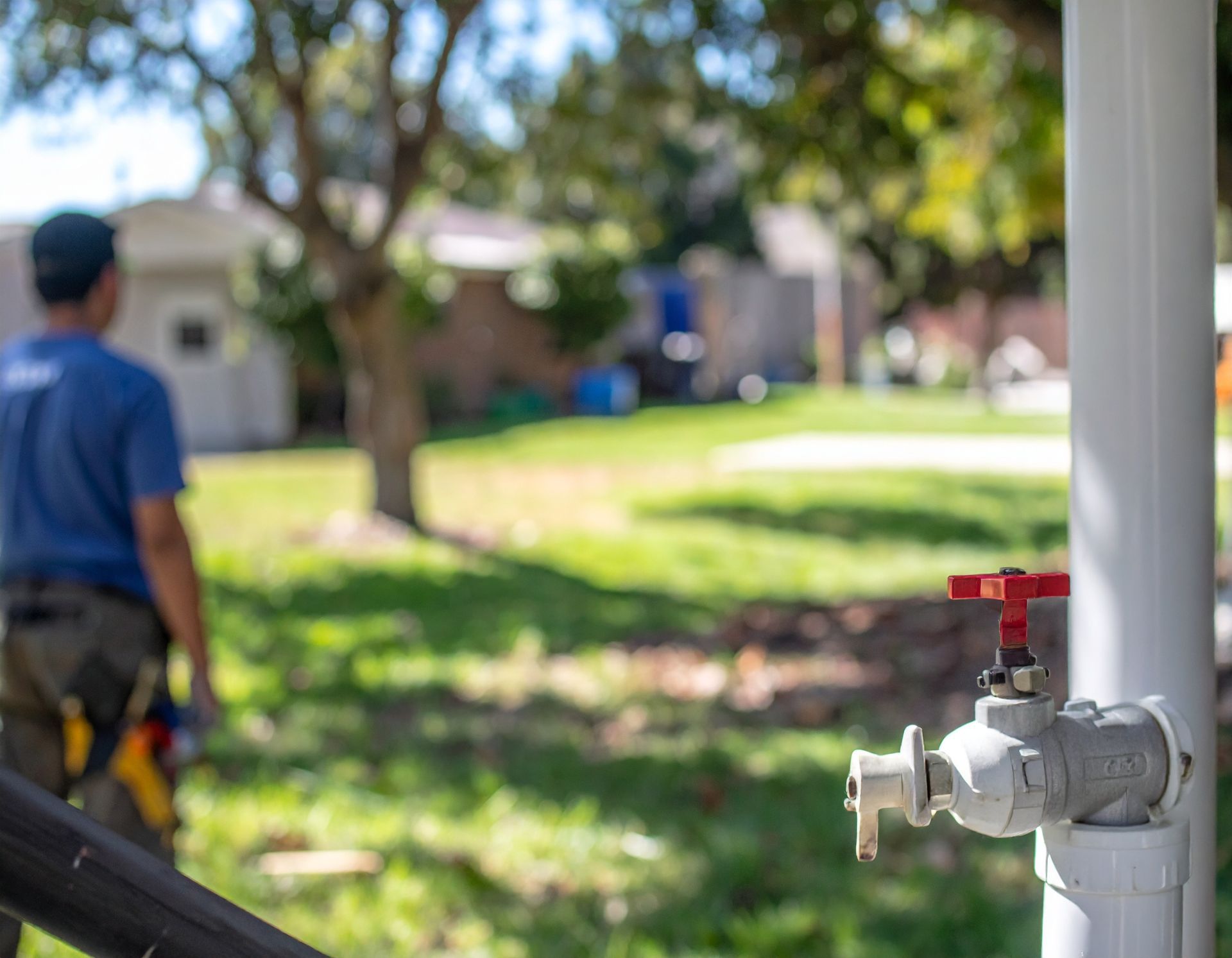 Plumber in blue uniform repairing an outdoor water pipe beside a house