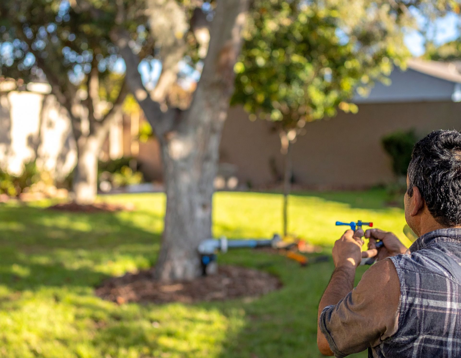 Person aiming a toy dart gun in a sunny backyard with a tree and house in the background