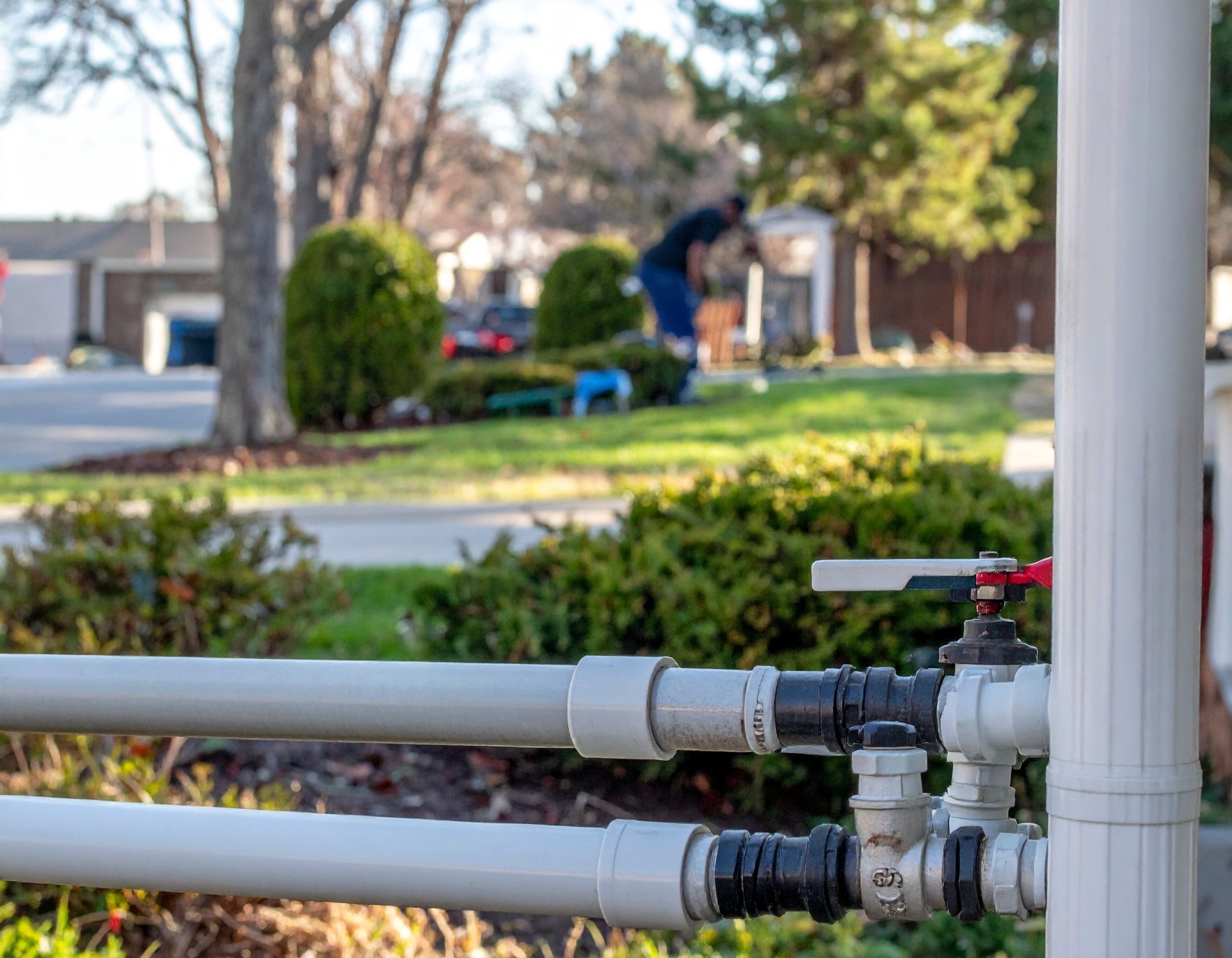 White pipes and valves in a yard with a blurred worker in the background