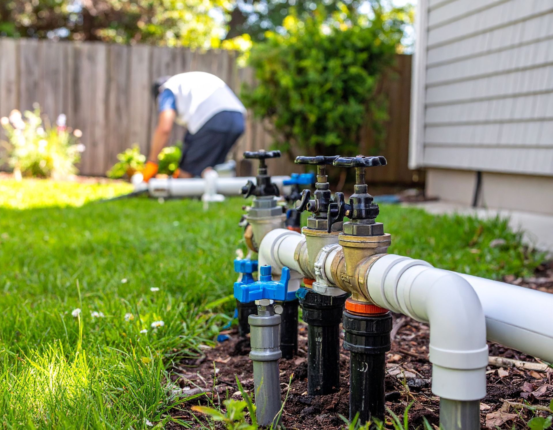 Garden irrigation pipes and valves in a lawn, with a worker crouched in the background.