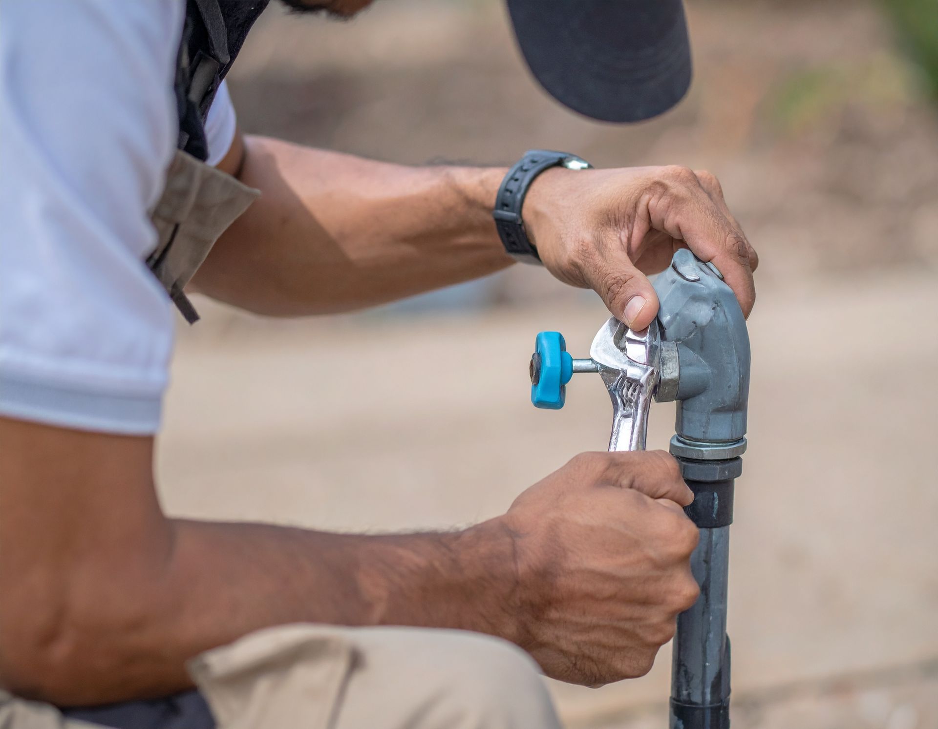 Person turning a blue valve on a gray outdoor water pipe