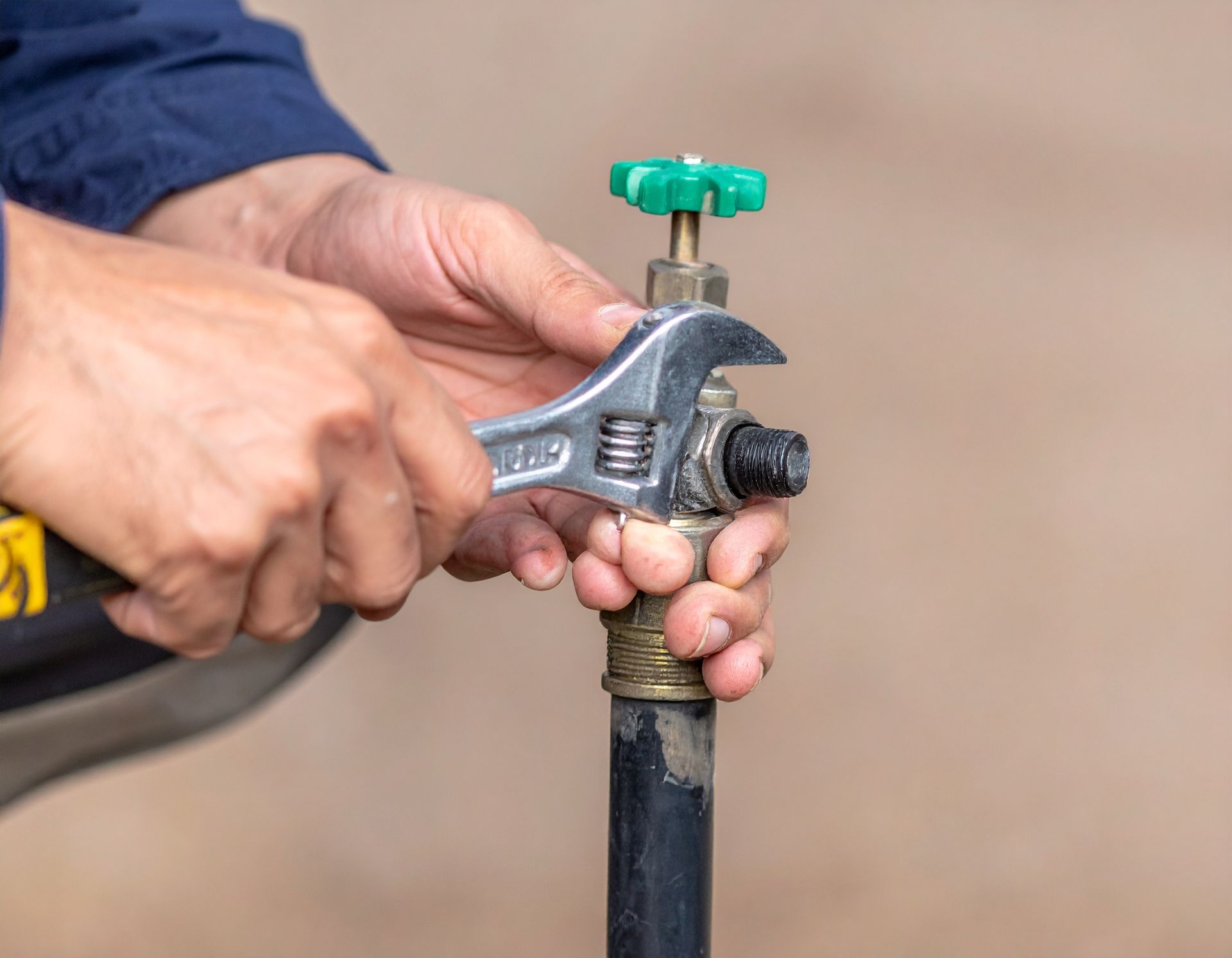 Hands using a metal hose spigot with a green valve handle outdoors.
