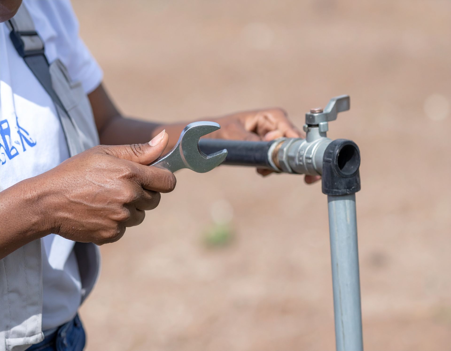 Hands using a wrench to tighten a metal pipe fitting outdoors