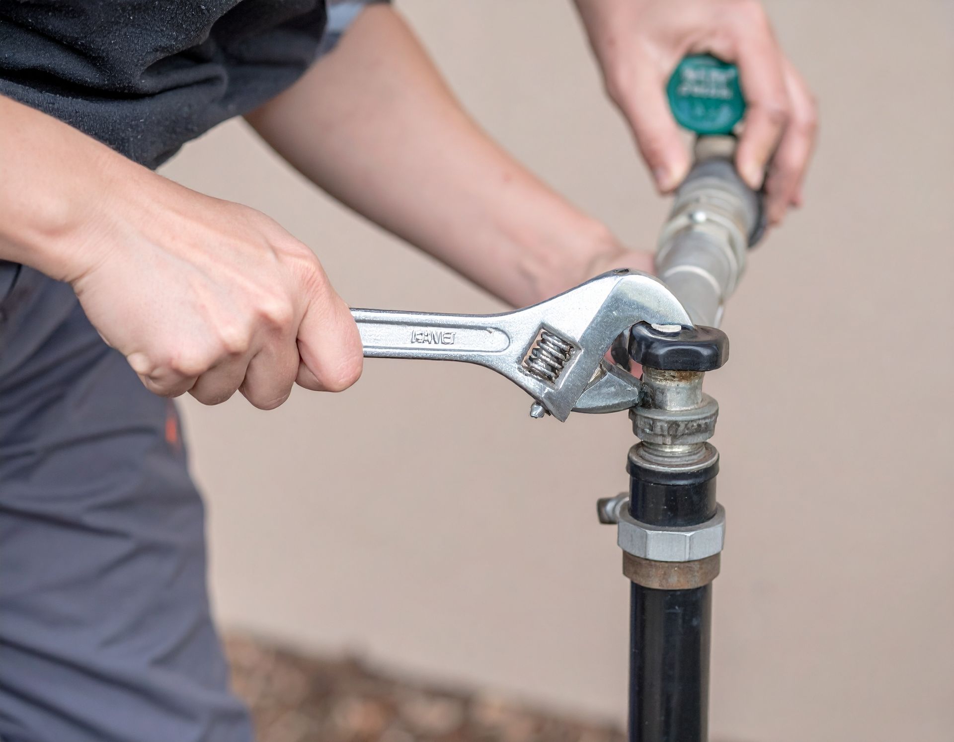 Hands using a wrench to tighten a metal pipe connection indoors