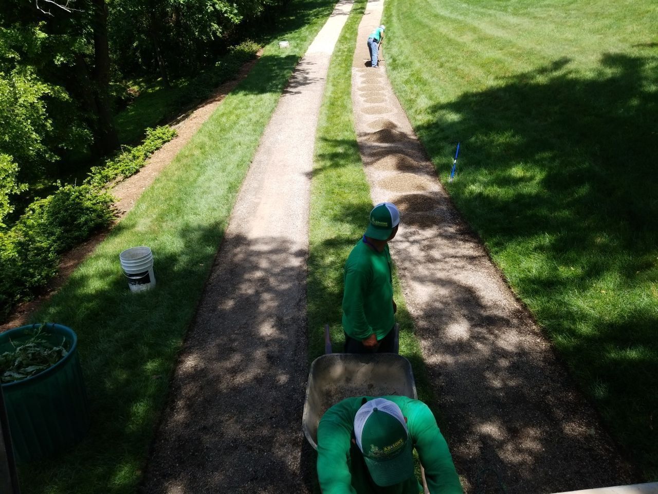 Two men in green uniforms are working on a driveway.