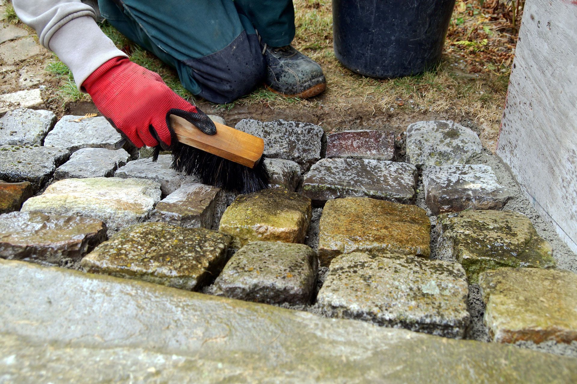 Person in red gloves brushes grout between cobblestones near a cement border.