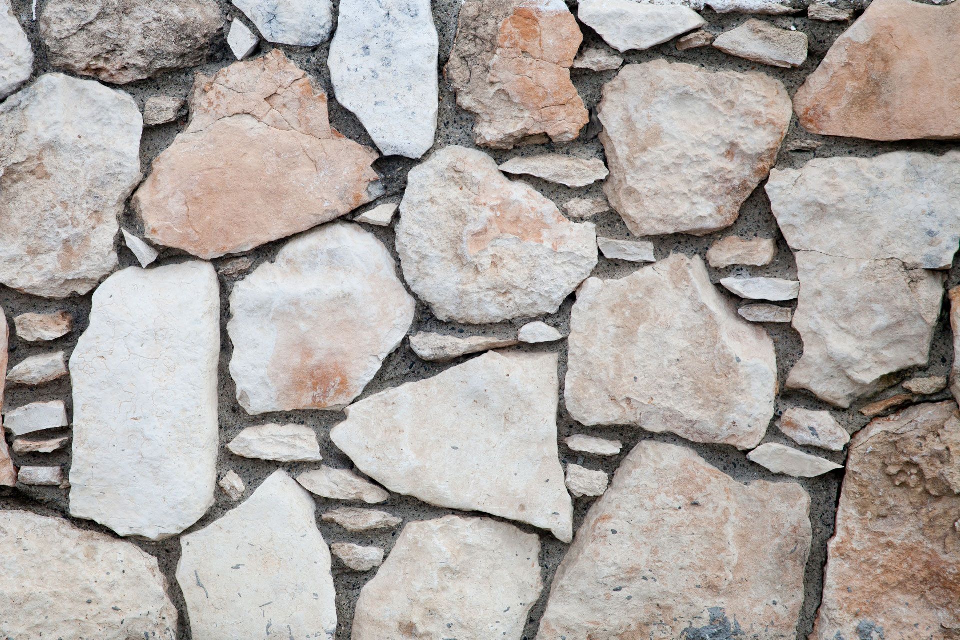 Stone wall with irregularly shaped, beige and gray stones, set in dark mortar.