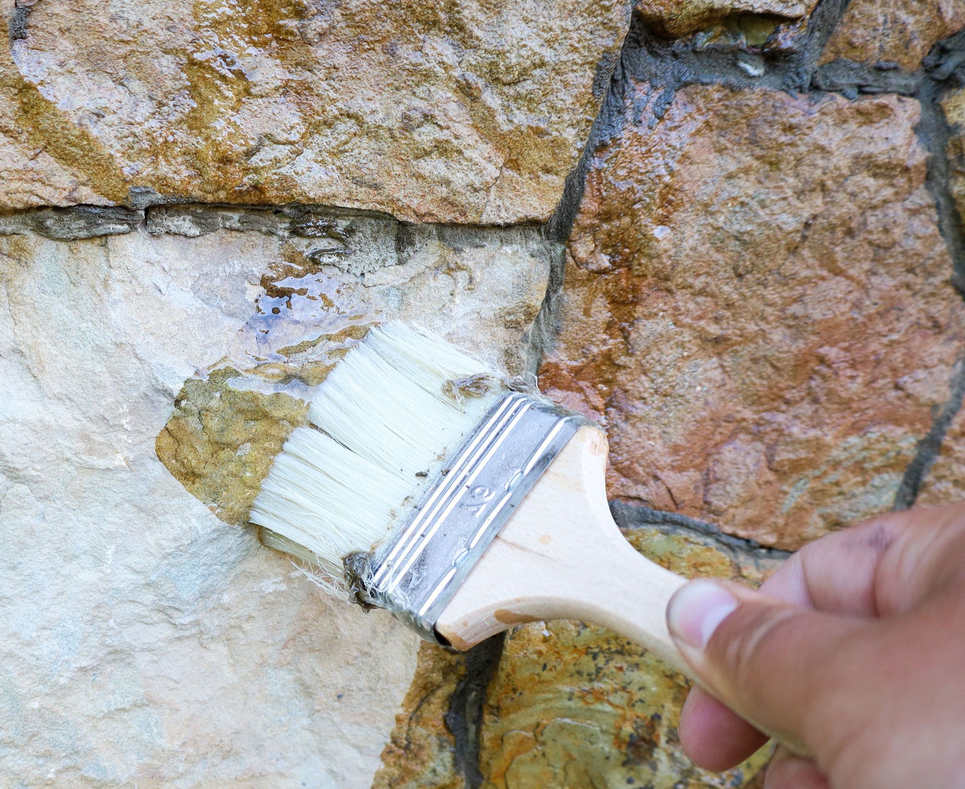 Hand applying sealant to stone wall with a paintbrush; exterior setting.