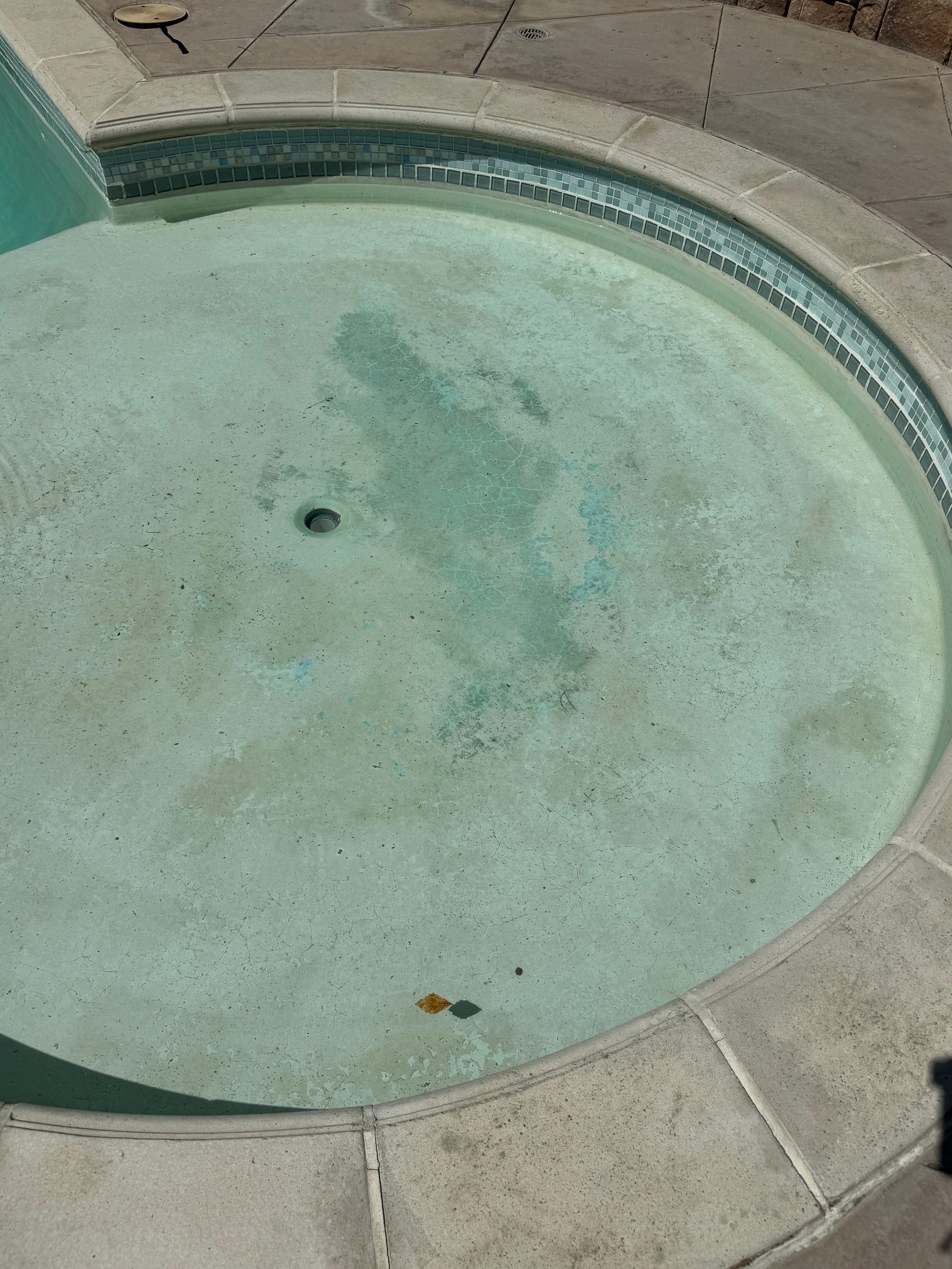 A dirty flooring of a circular swimming pool with a drain hole in the middle of it.