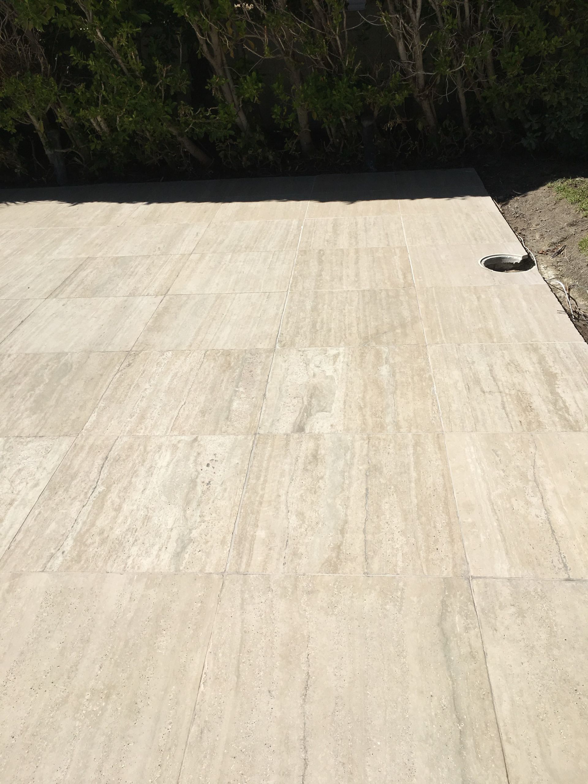 Beige tile patio, leading to a green hedge. Sunlight.